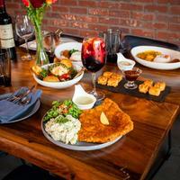 Dinner table with various dishes, a glass of red wine, and a brick wall background.