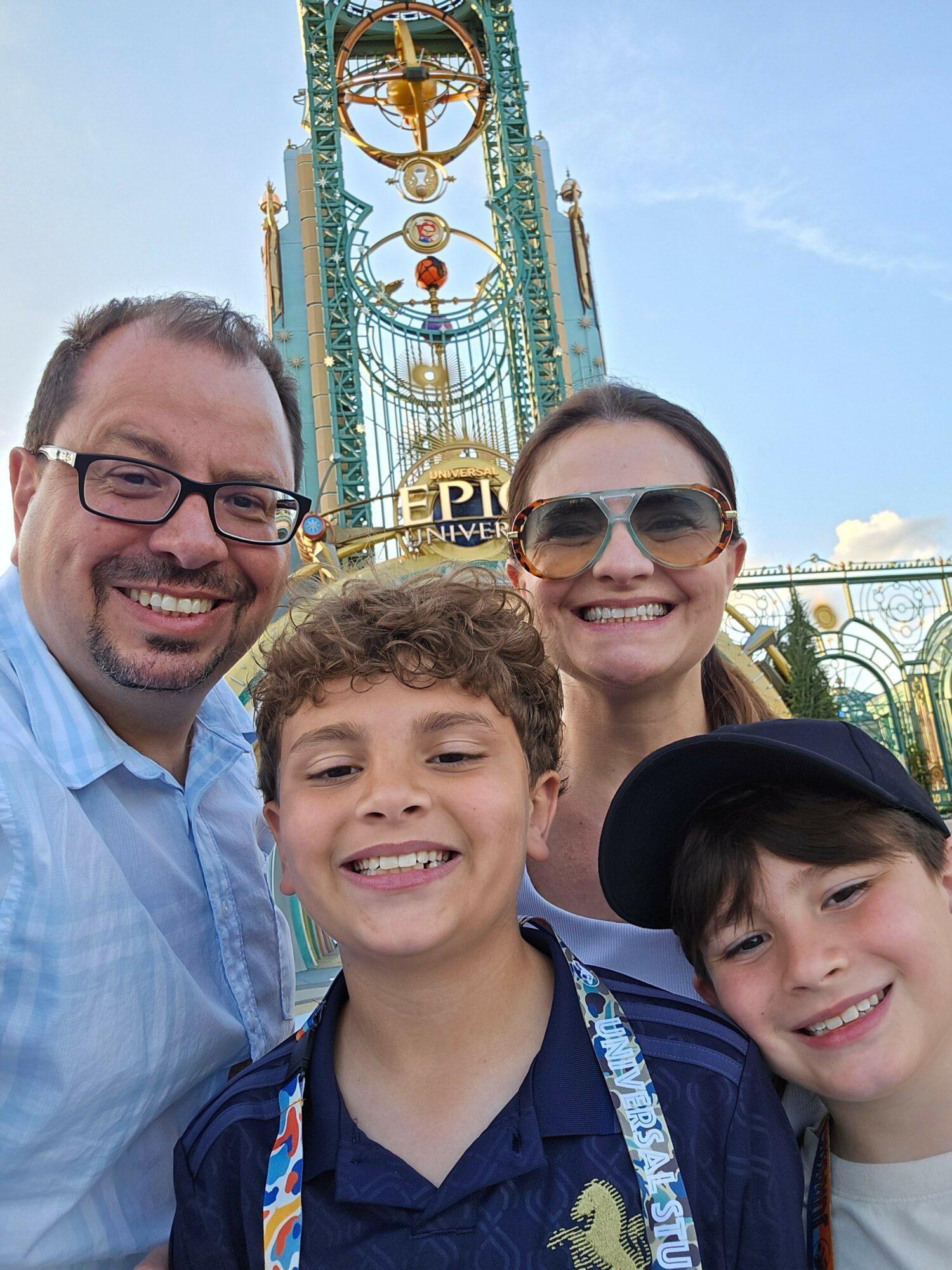Four people smiling in front of a colorful amusement park ride with a tall tower and decorative elements.
