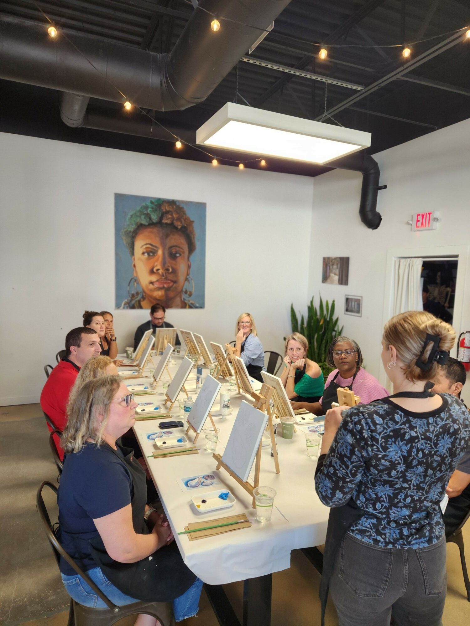 People gathered around a table with jewelry displays, in a room with artwork on the wall.