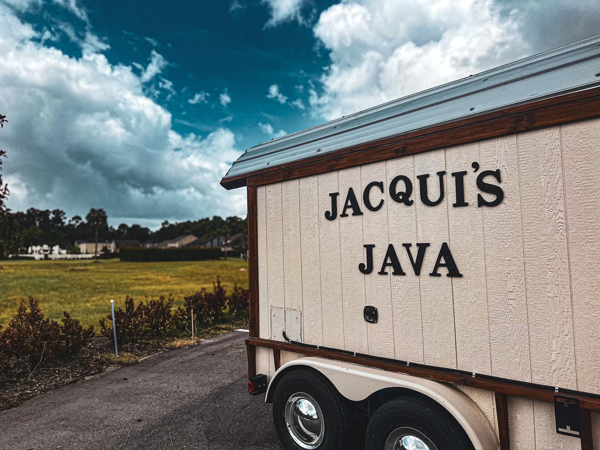 Building with sign reading 'JACQUI'S JAVA' against a cloudy sky and open field background.