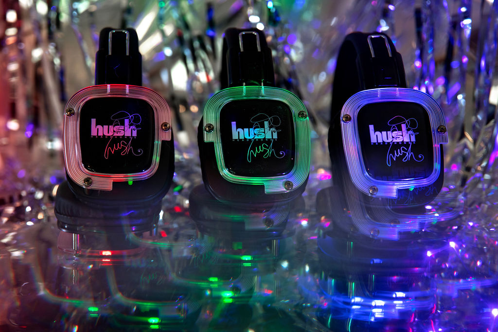 Three colorful wristwatches with digital displays are displayed on a reflective surface with colorful lights in the background.