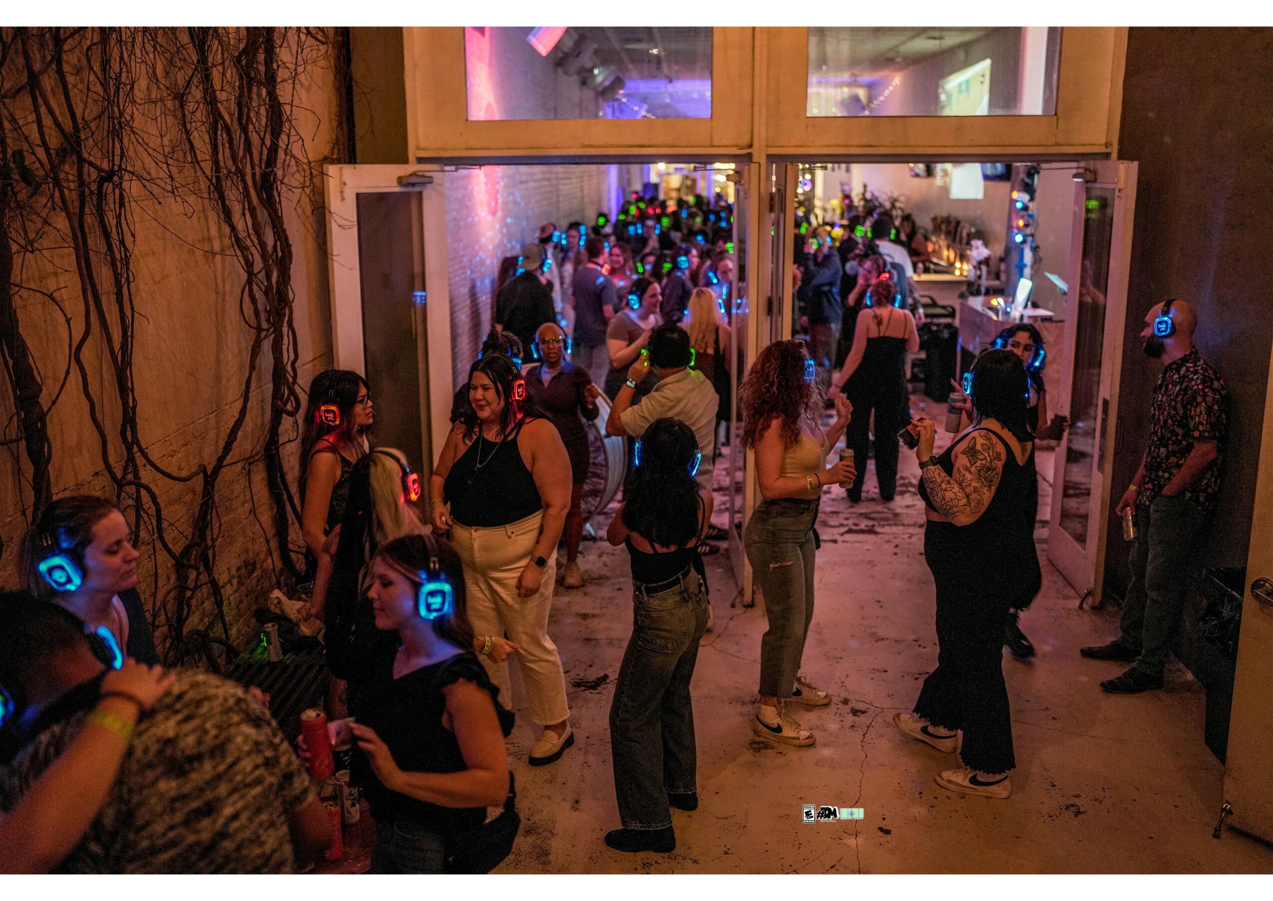 People wearing headphones gather near an entrance, with a crowd visible inside a dimly lit venue.