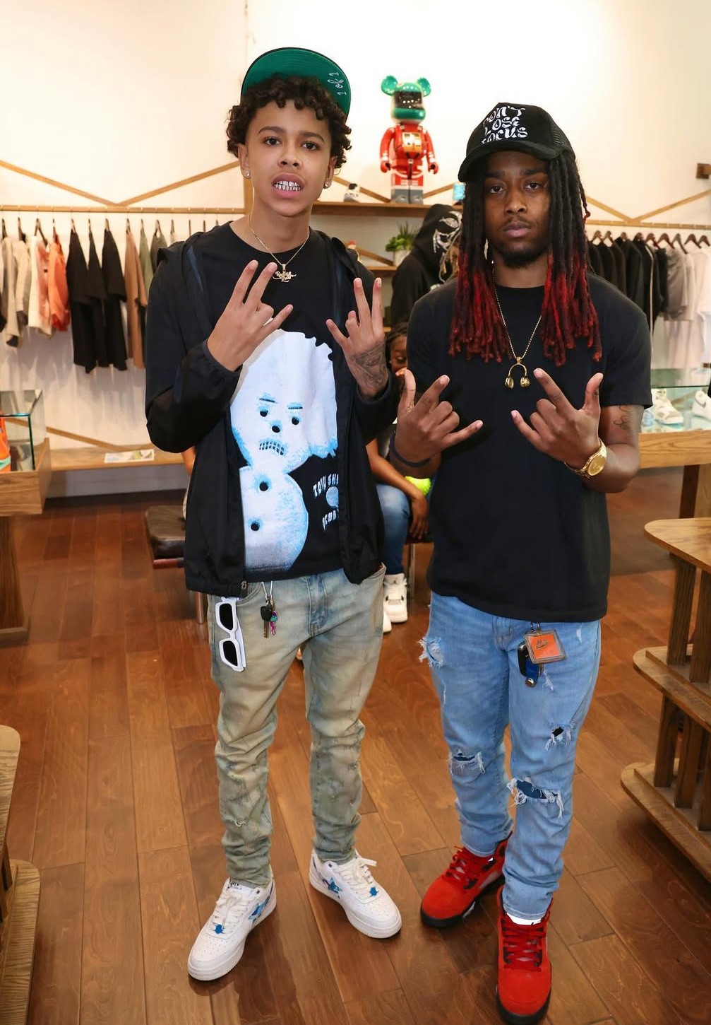 Two young people standing in a clothing store, making hand gestures, with racks of clothes behind them.