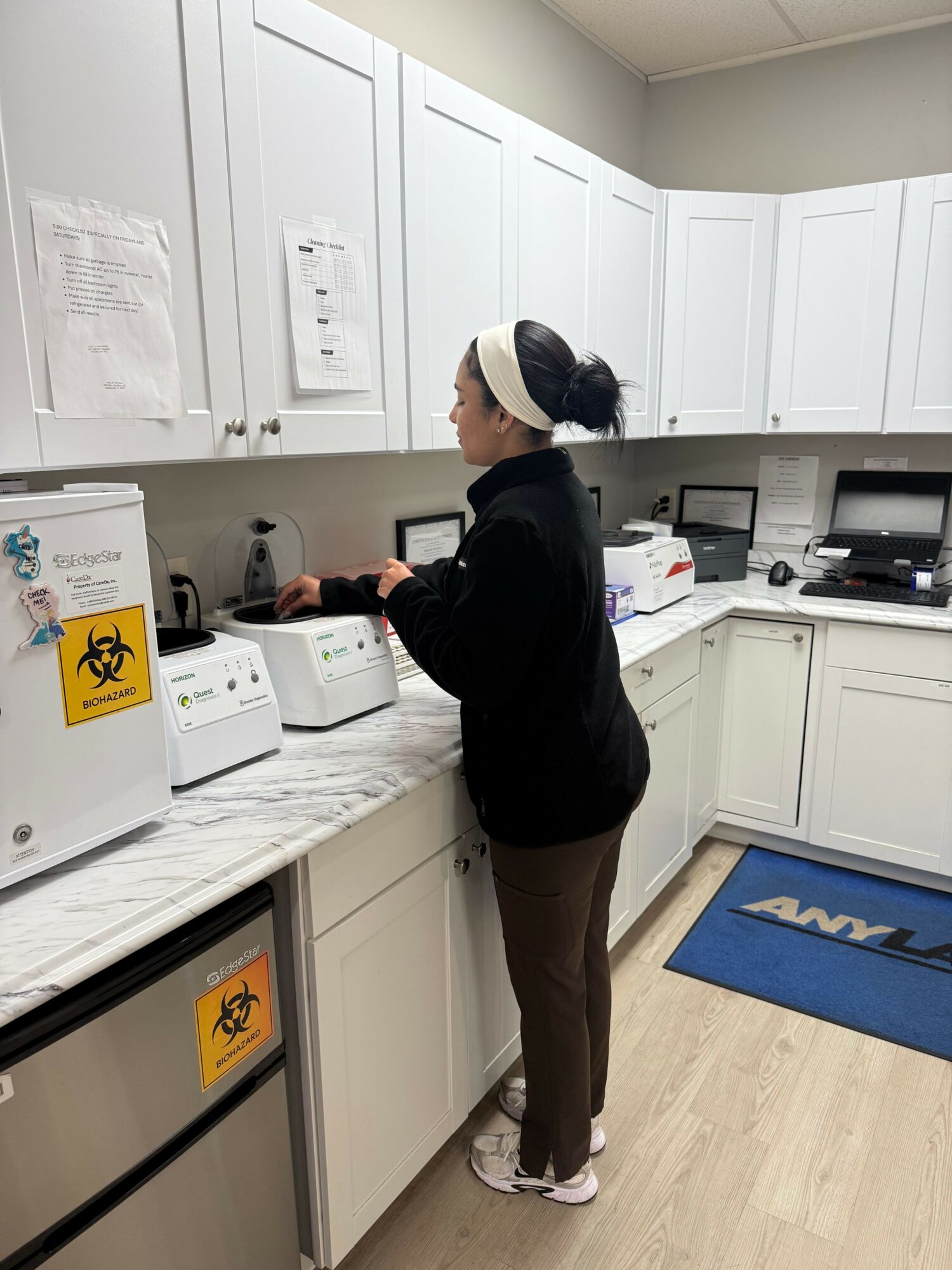 Person standing in a kitchen, using a microwave, with white cabinets and a blue mat on the floor.
