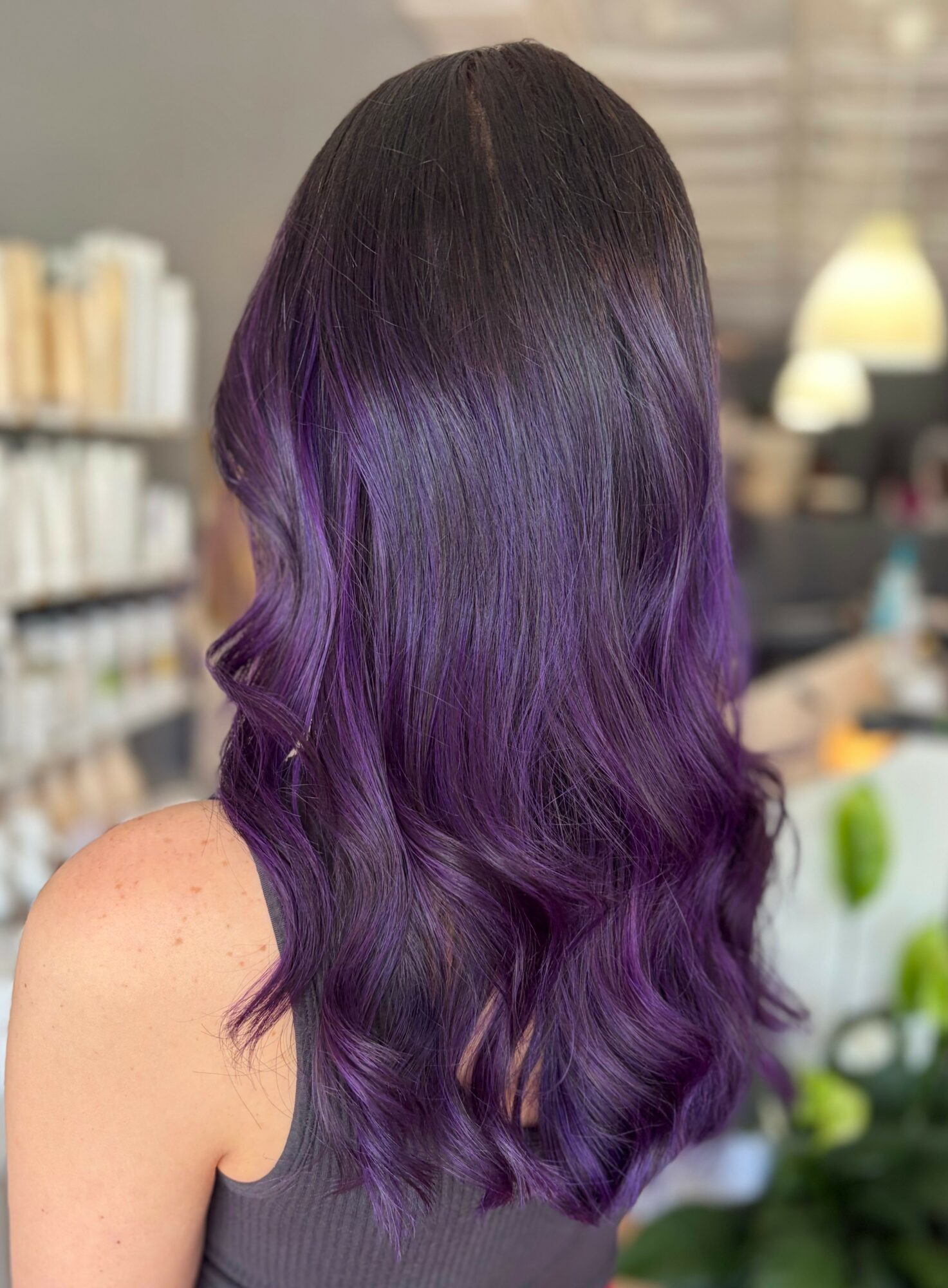 Back view of a woman with long, wavy hair transitioning from dark brown to vibrant purple.