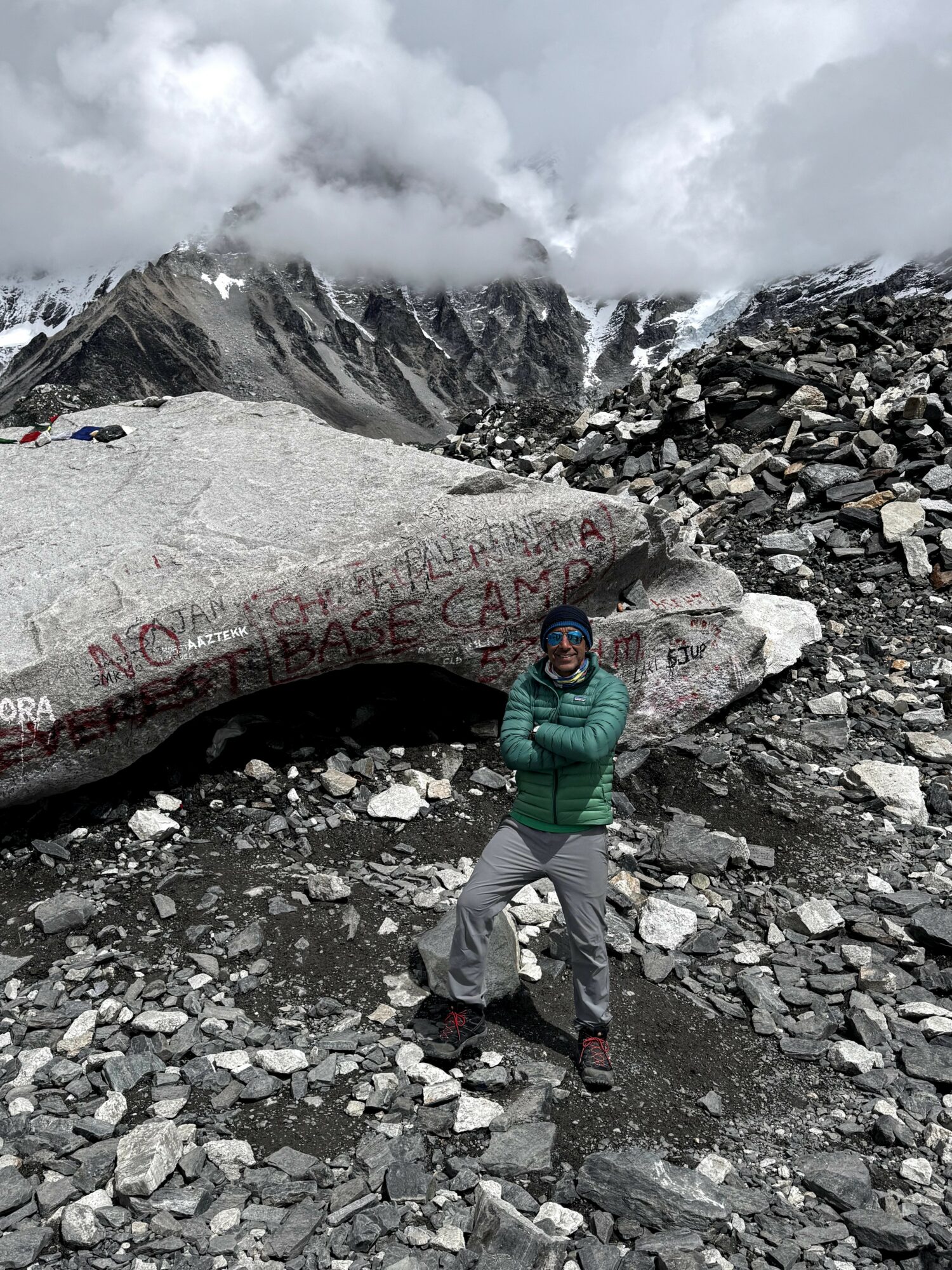 Person standing on rocky terrain with mountains and cloudy sky in background.