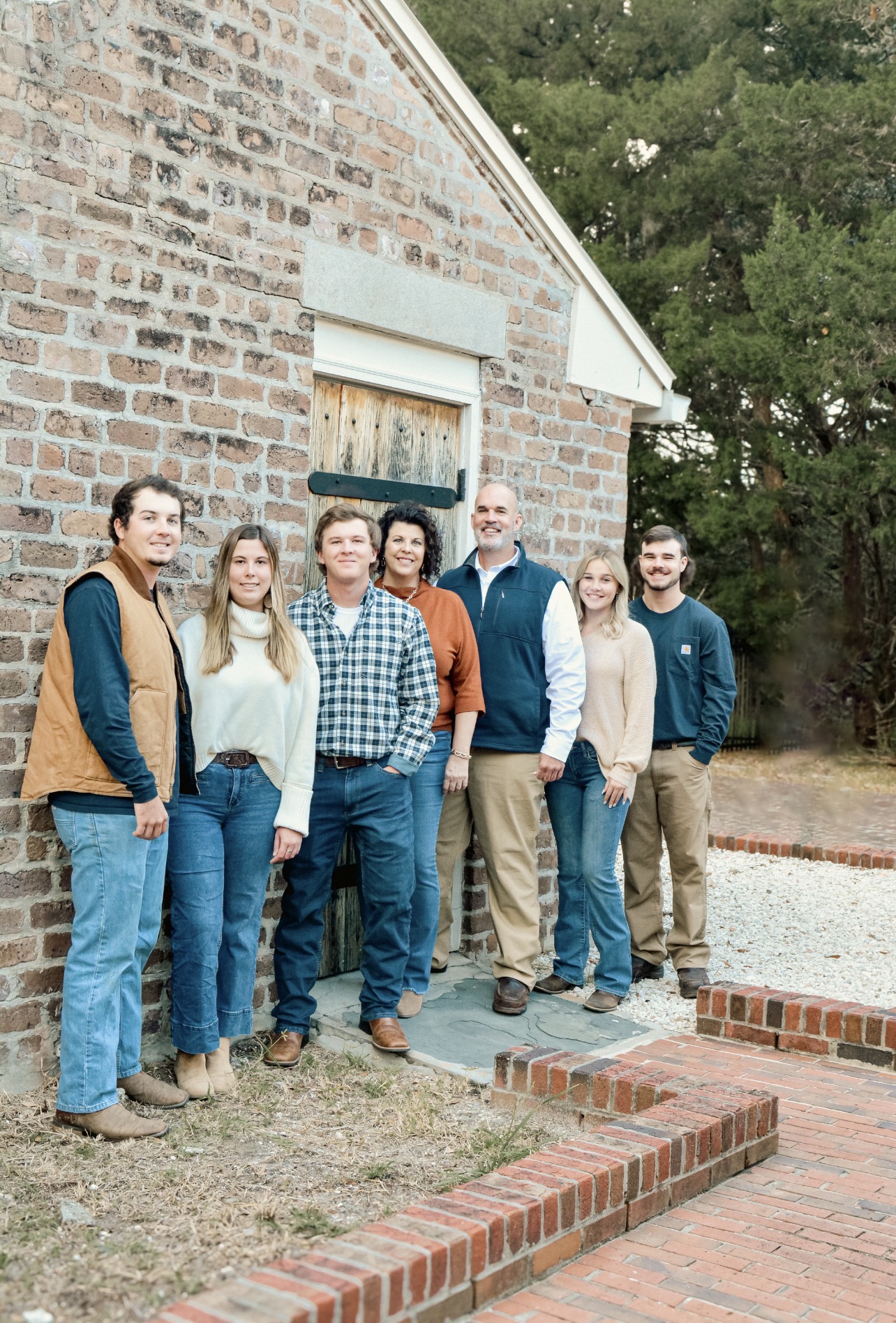 Group of six people standing outside a brick building with trees in the background.