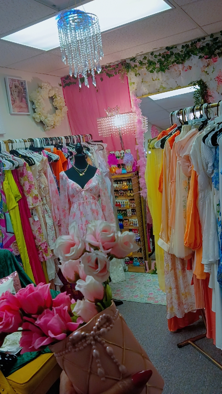 Clothing store with colorful dresses, pink flowers, and a chandelier, viewed from a low angle.