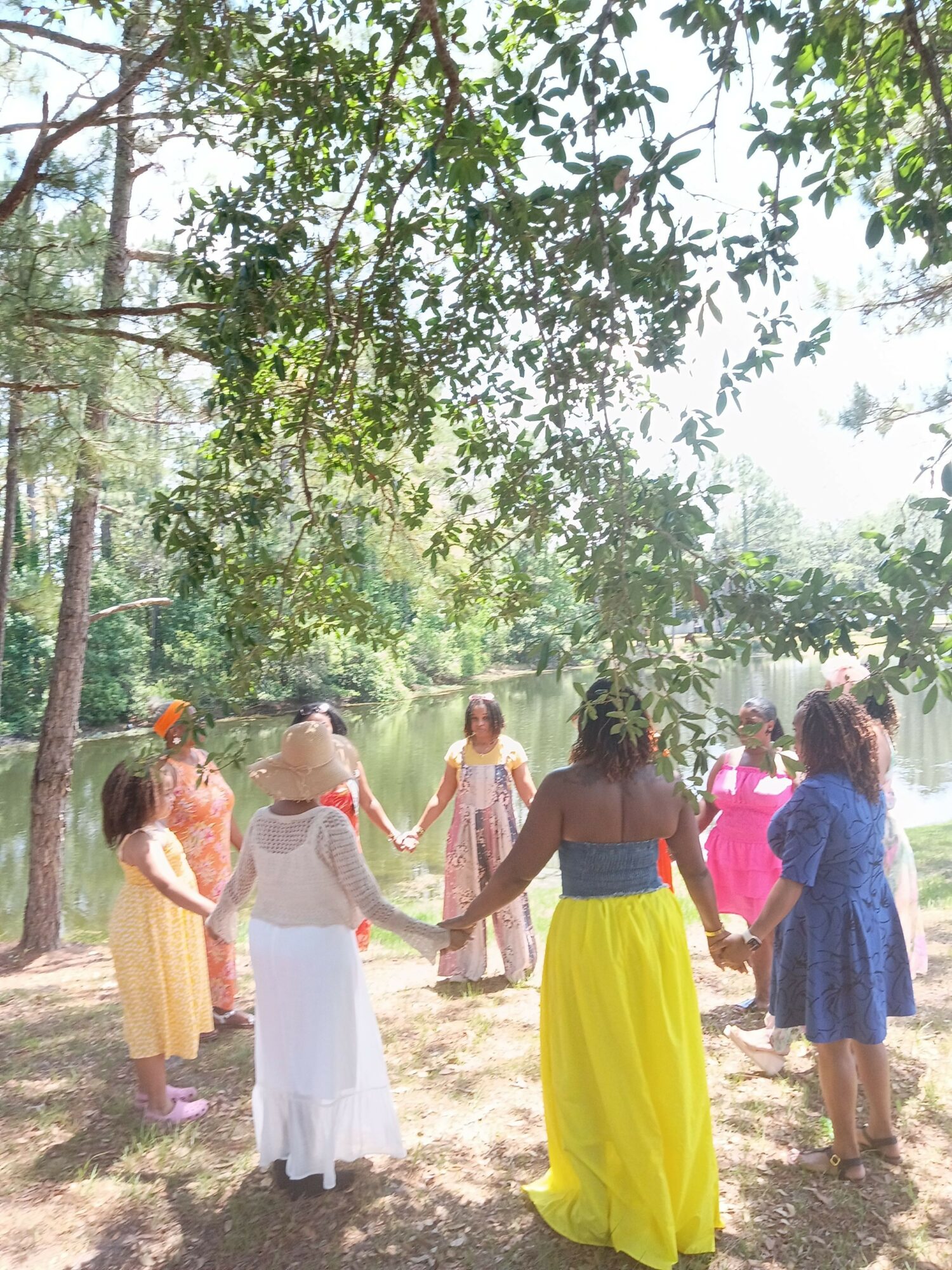Group of people walking outdoors among trees, some wearing colorful clothing, sunlight filtering through leaves.