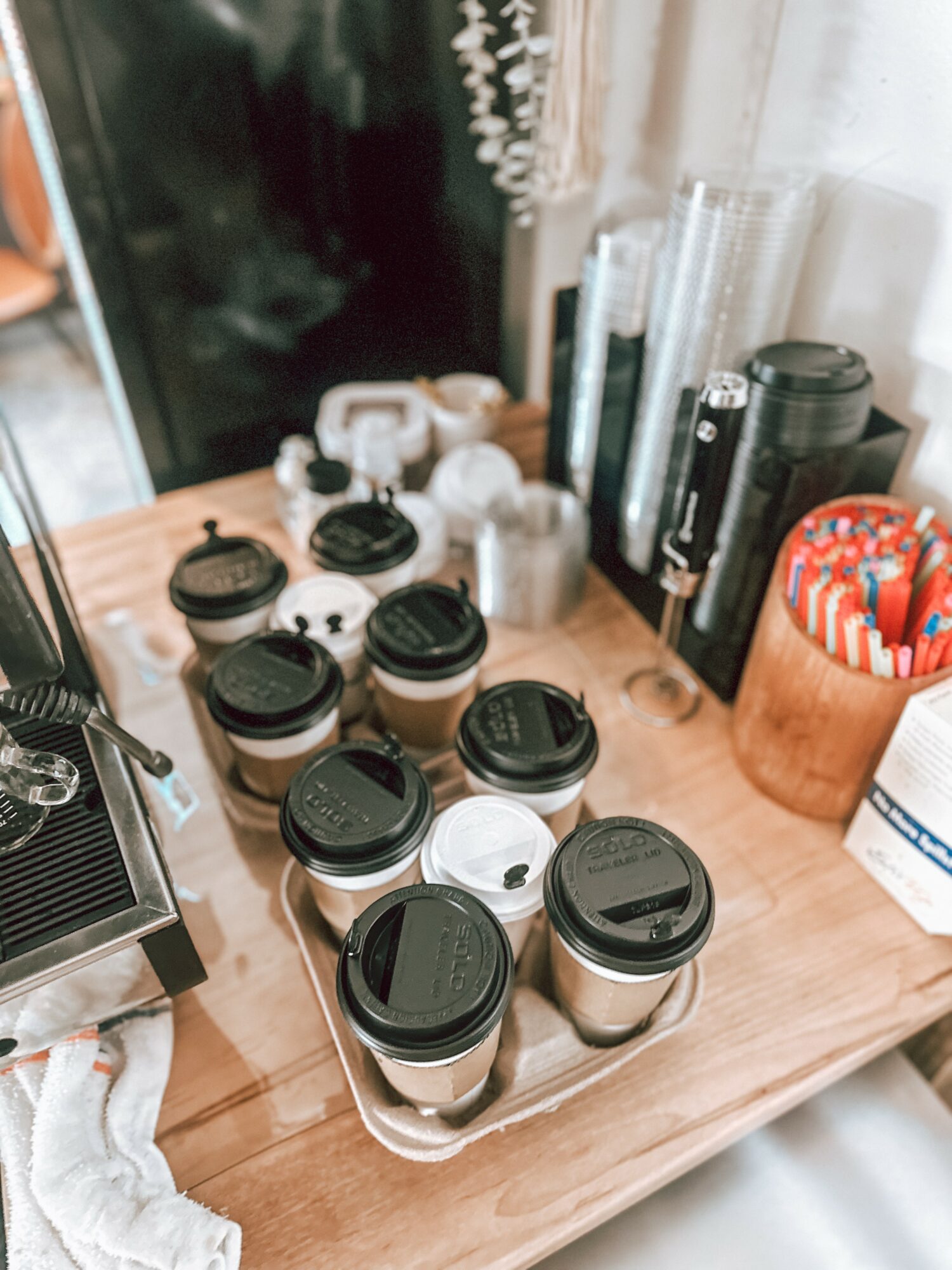 Coffee cups and various containers on a wooden table, with a dark background and a window. Word count: 20.