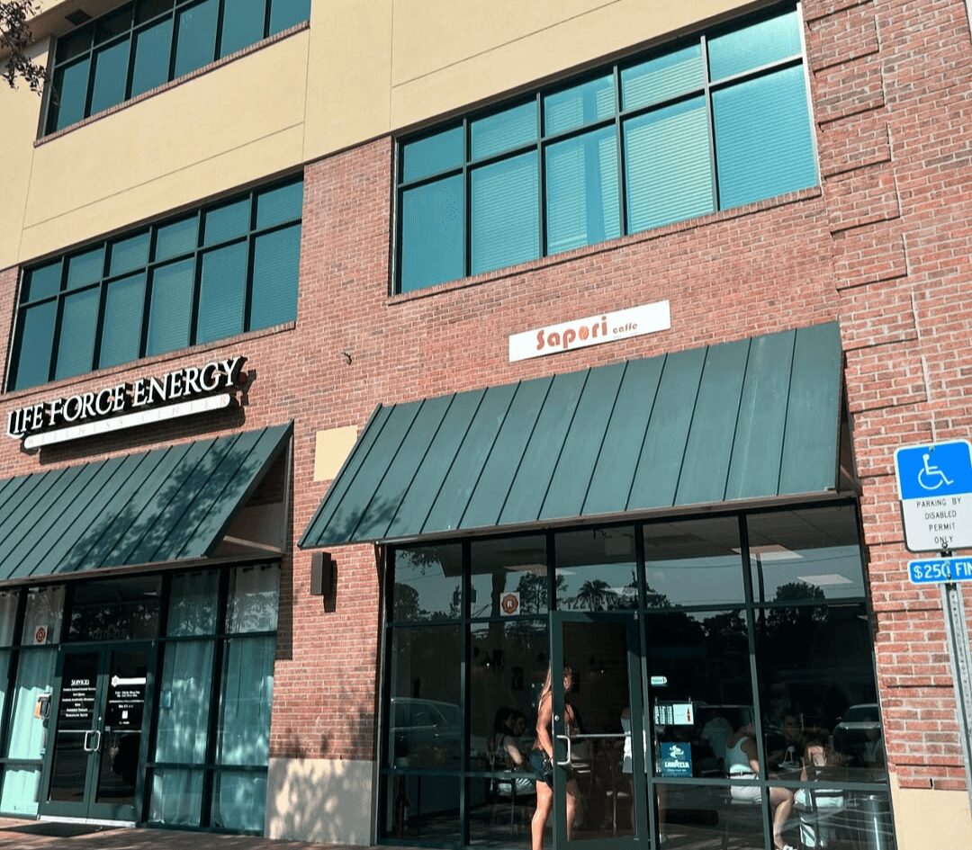 Building with large windows, storefronts, and a woman standing outside, with a blue handicap parking sign nearby.