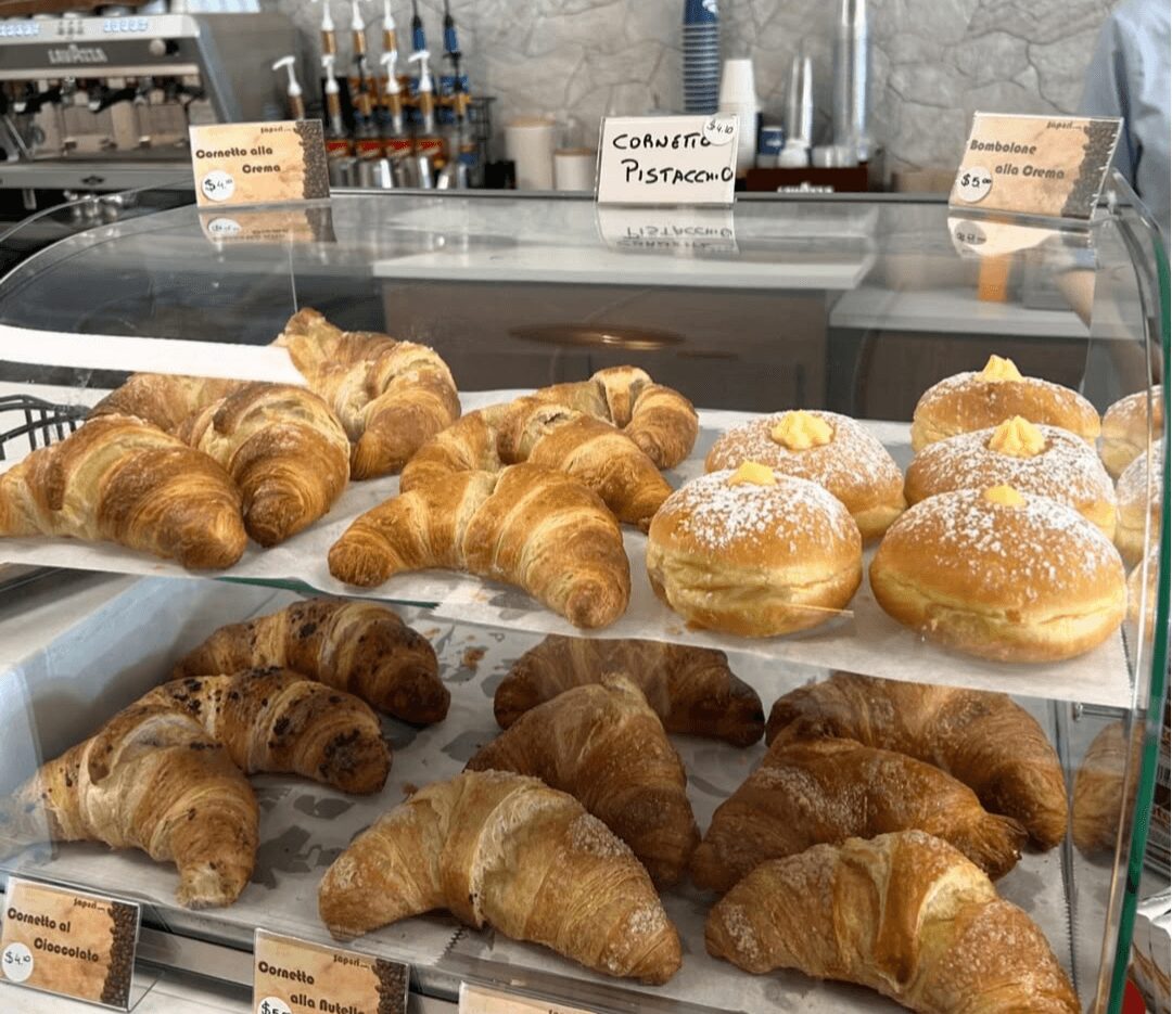 Display case with croissants and round pastries topped with powdered sugar, in a bakery setting.