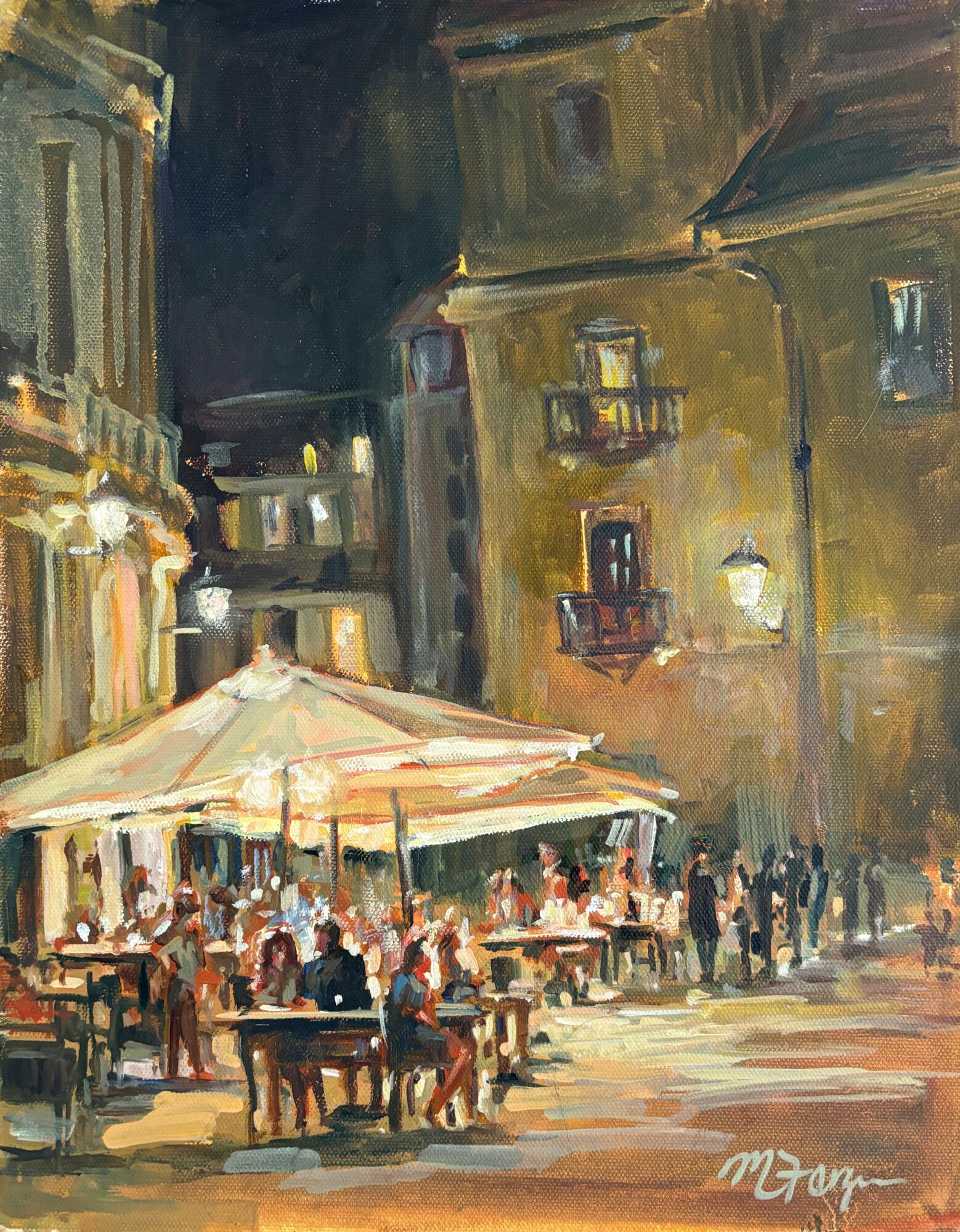 Night scene of a lively outdoor café with people sitting at tables under umbrellas, surrounded by tall buildings with lit windows.