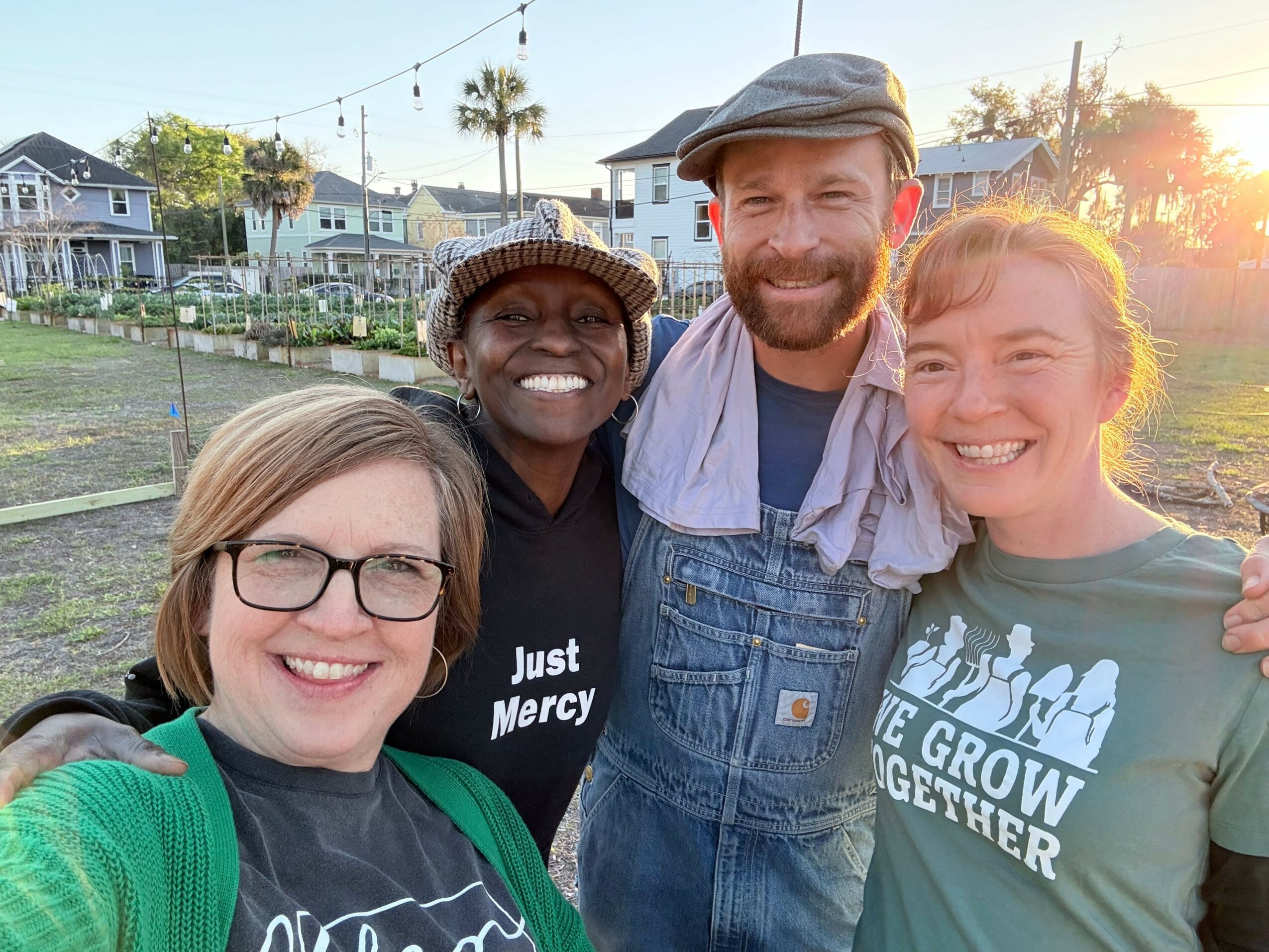 Four people smiling and taking a selfie outdoors, with houses and trees in the background.