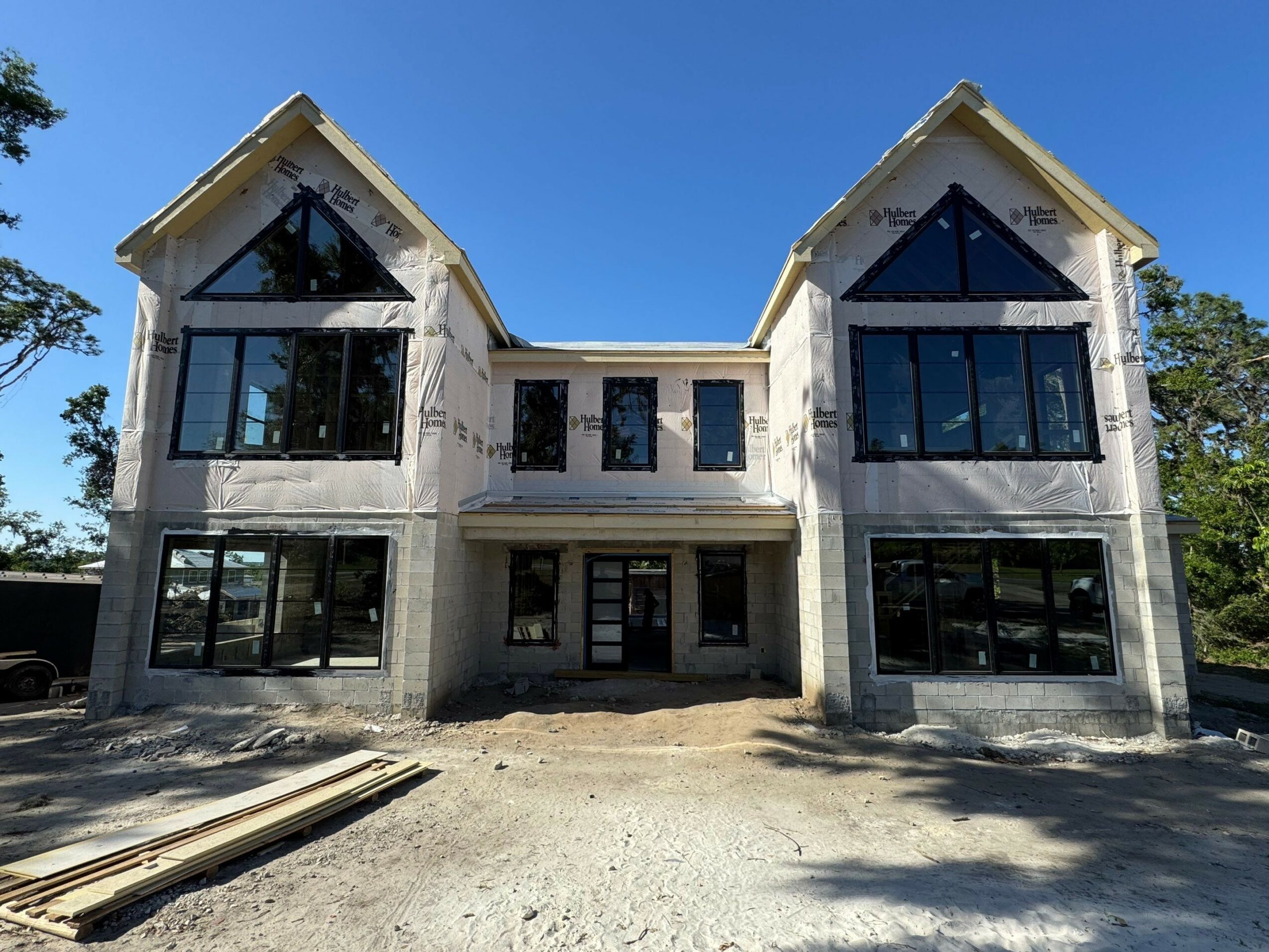 Newly constructed house with large windows and a central entrance, set against a clear blue sky.