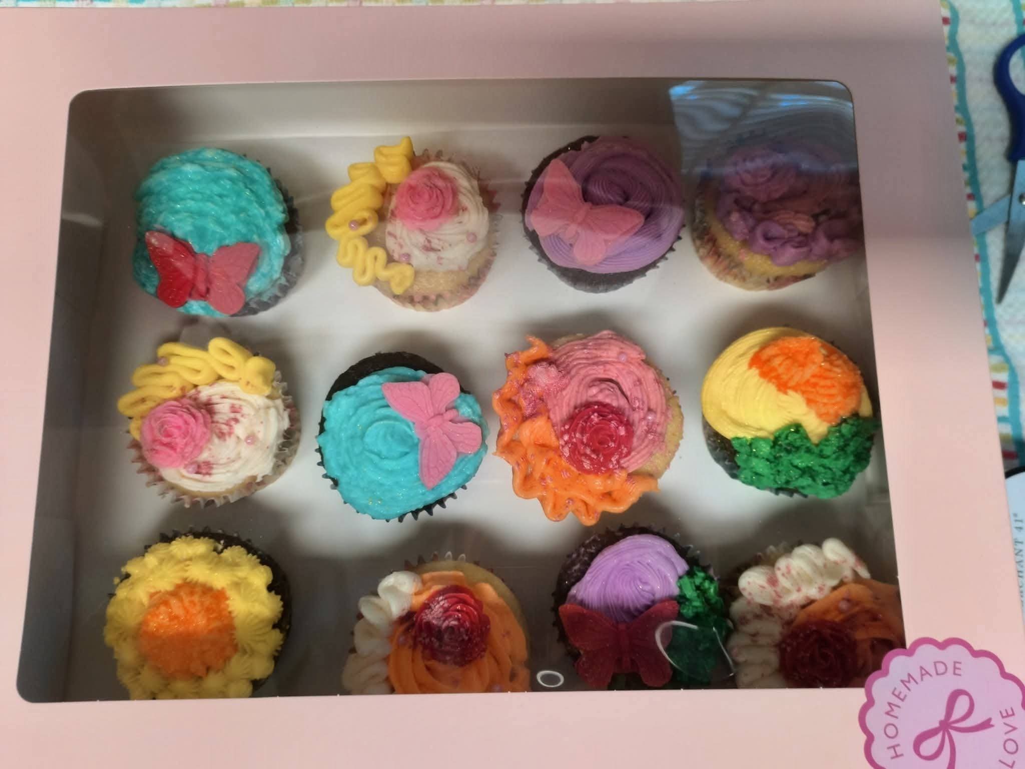 Box of twelve decorated cupcakes with colorful frosting and toppings, arranged in three rows of four.