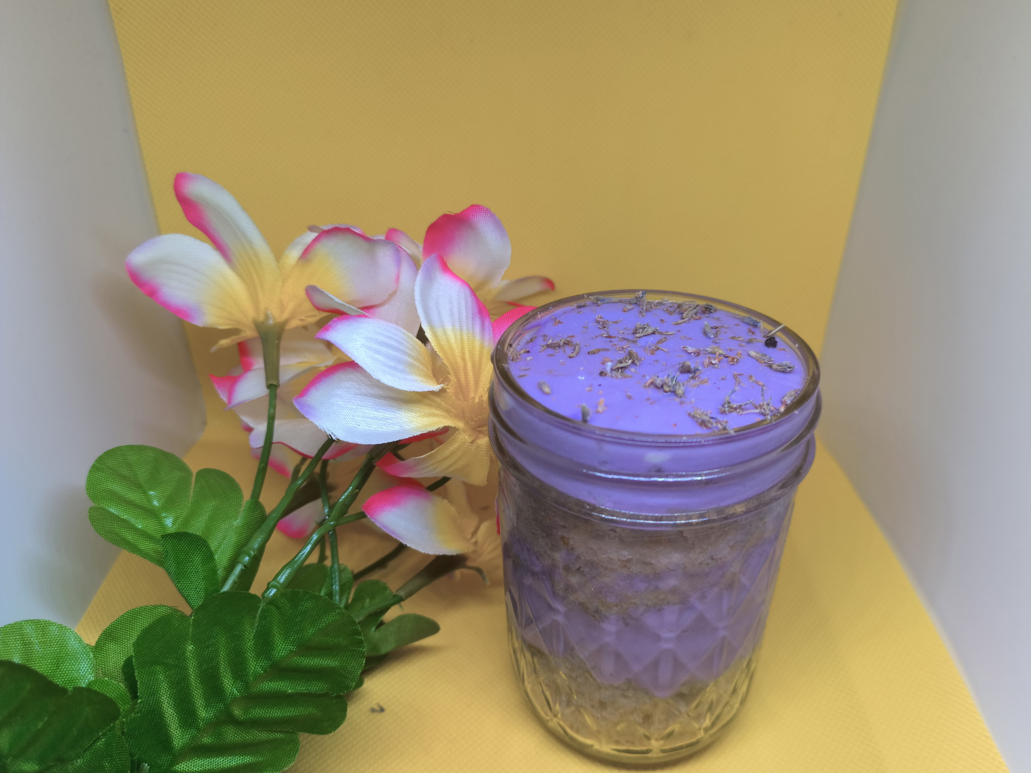 A purple jar with a lid, flowers, and green leaves against a yellow background.