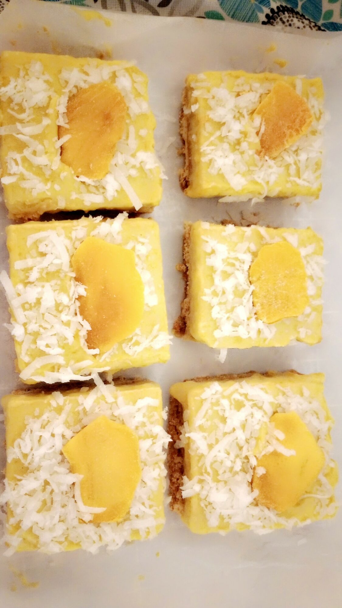 Six pieces of yellow cake with white frosting and a yellow filling, topped with shredded coconut, arranged on a white surface