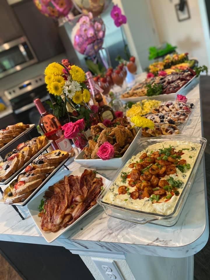 Table with various dishes, flowers, and drinks in a kitchen setting, viewed from an angle, with food and decorations visible.