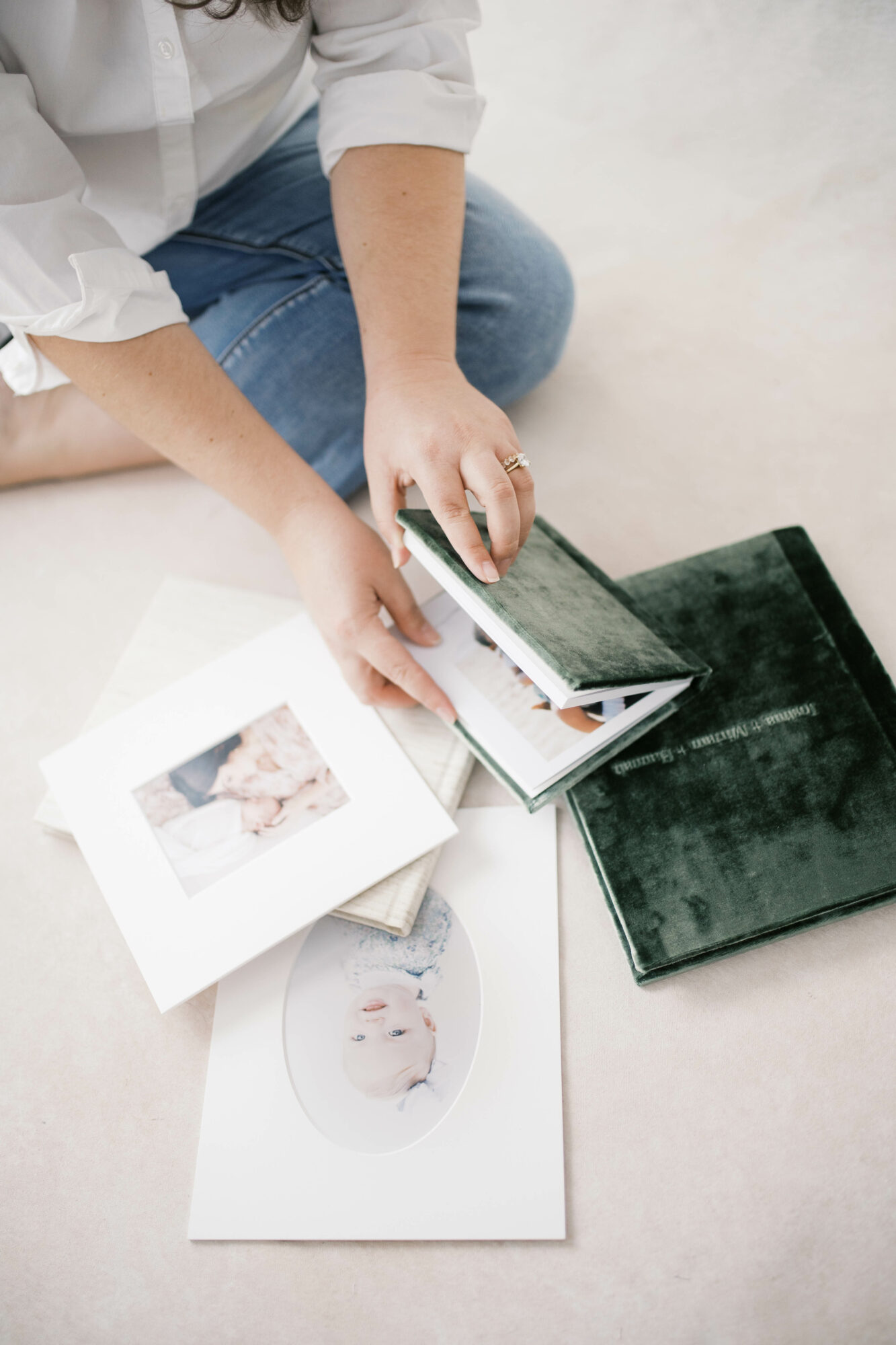 Person's hands flipping through photo albums on a white surface, with additional albums and printed photos nearby.