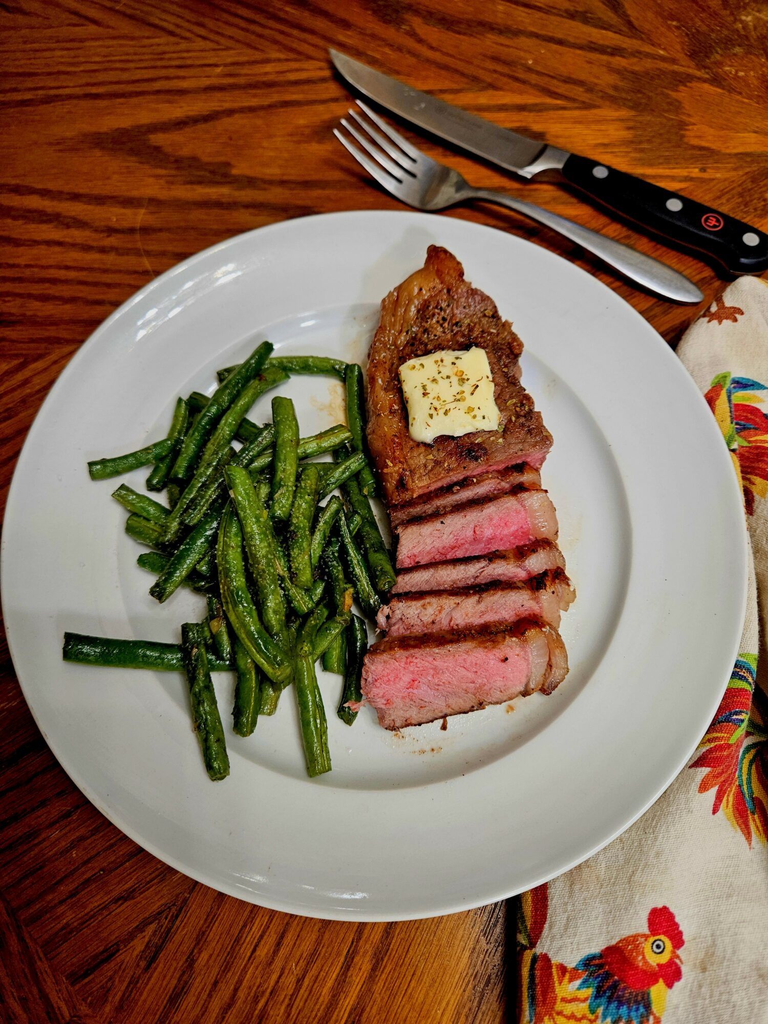 Steak with a pat of butter, sliced and cooked medium rare, served with green beans on a white plate.