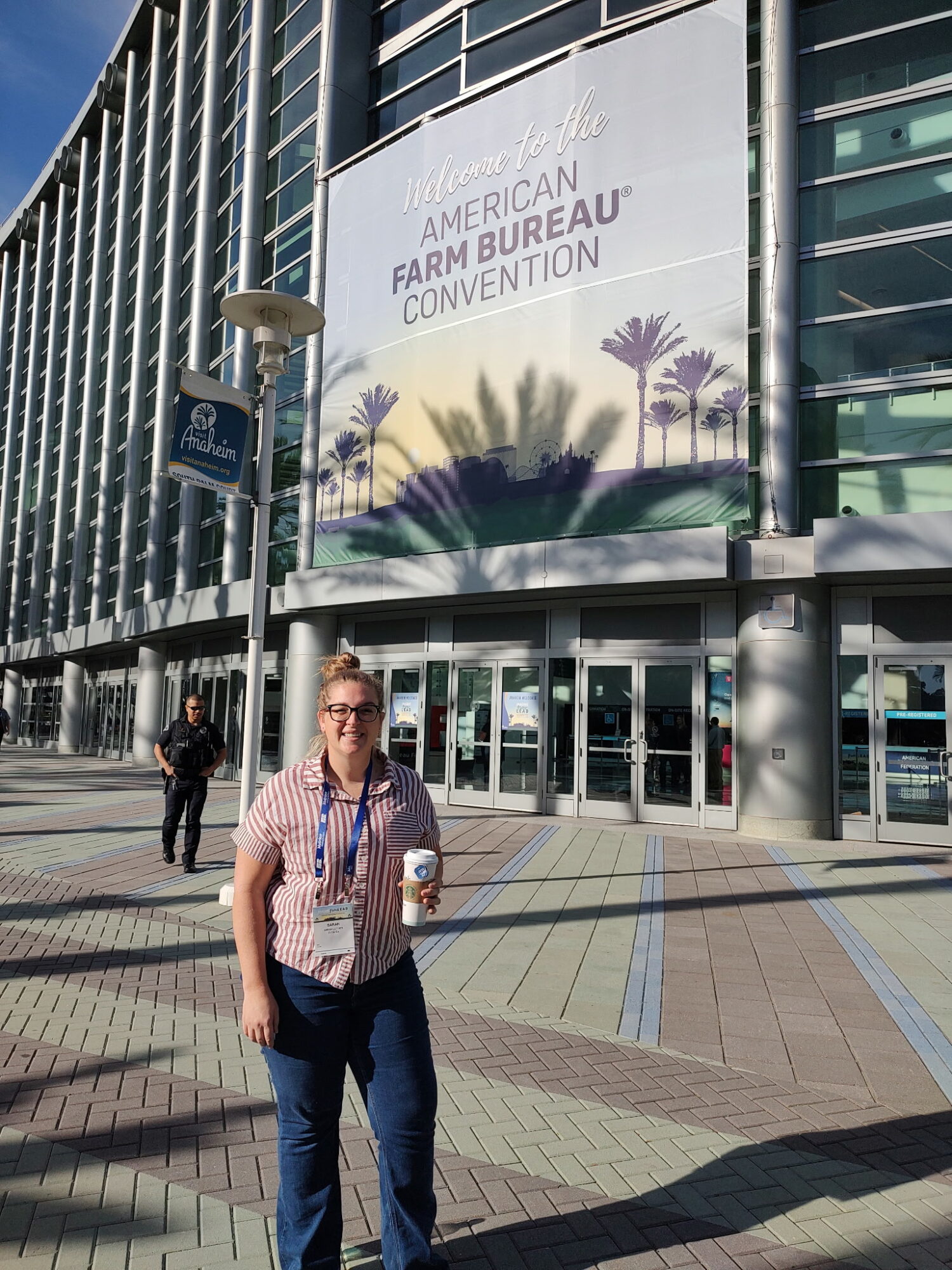 Person standing outside a large convention center with a banner for the American Farm Bureau Convention, holding a drink.