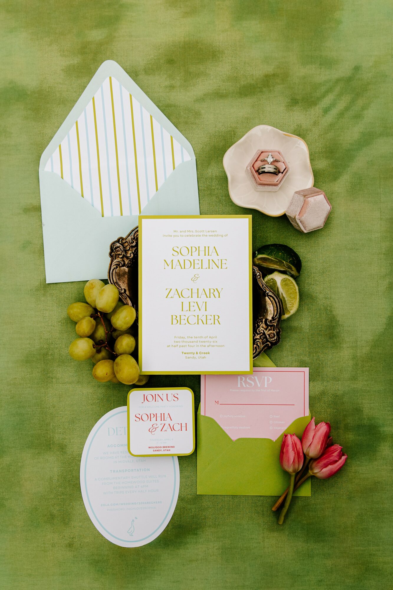 Open invitation card with yellow text, pink flowers, grapes, and small boxes on green background.