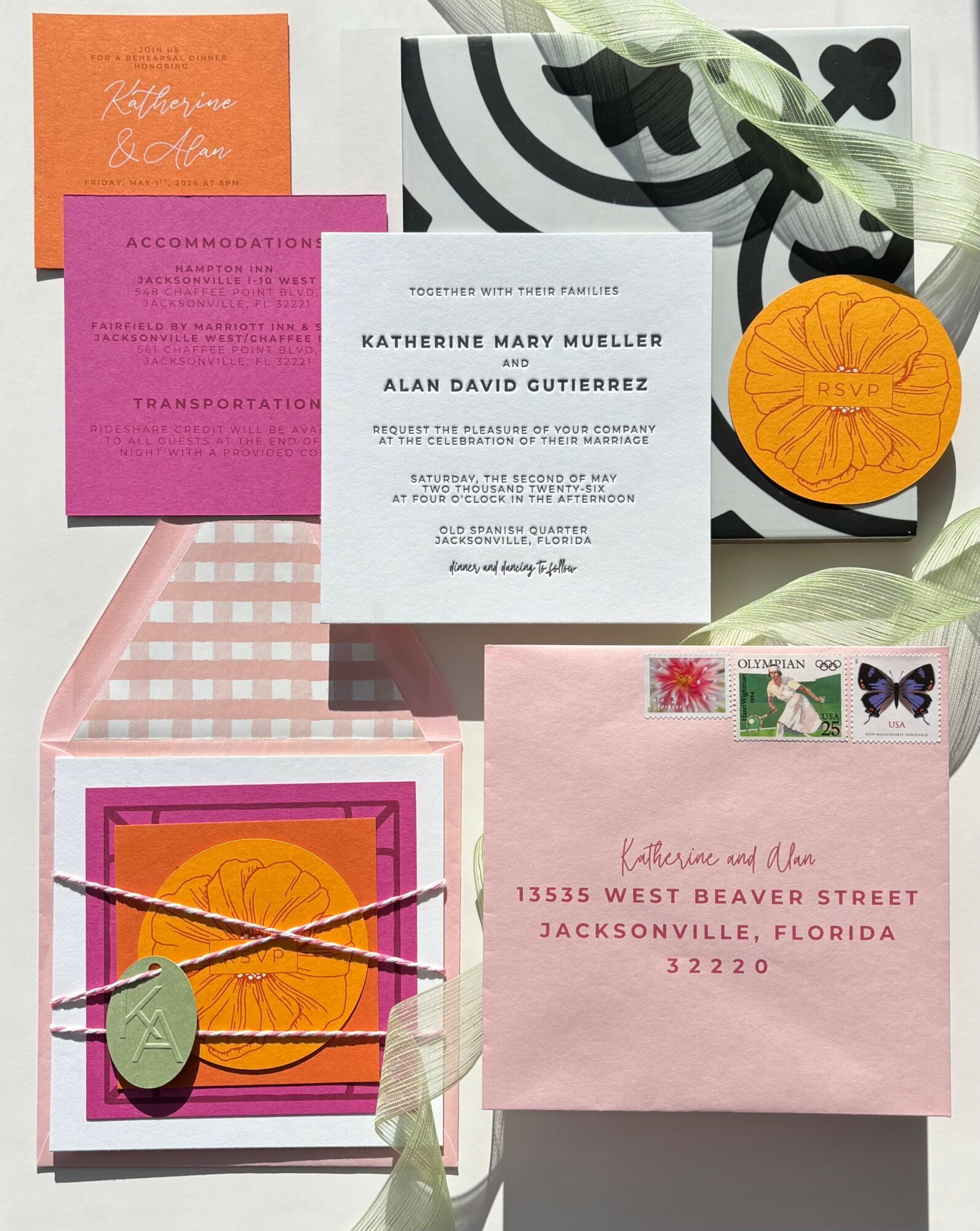 Flat lay of wedding invitations and cards with pink, orange, black, and white designs, some tied with ribbons, on a white background.