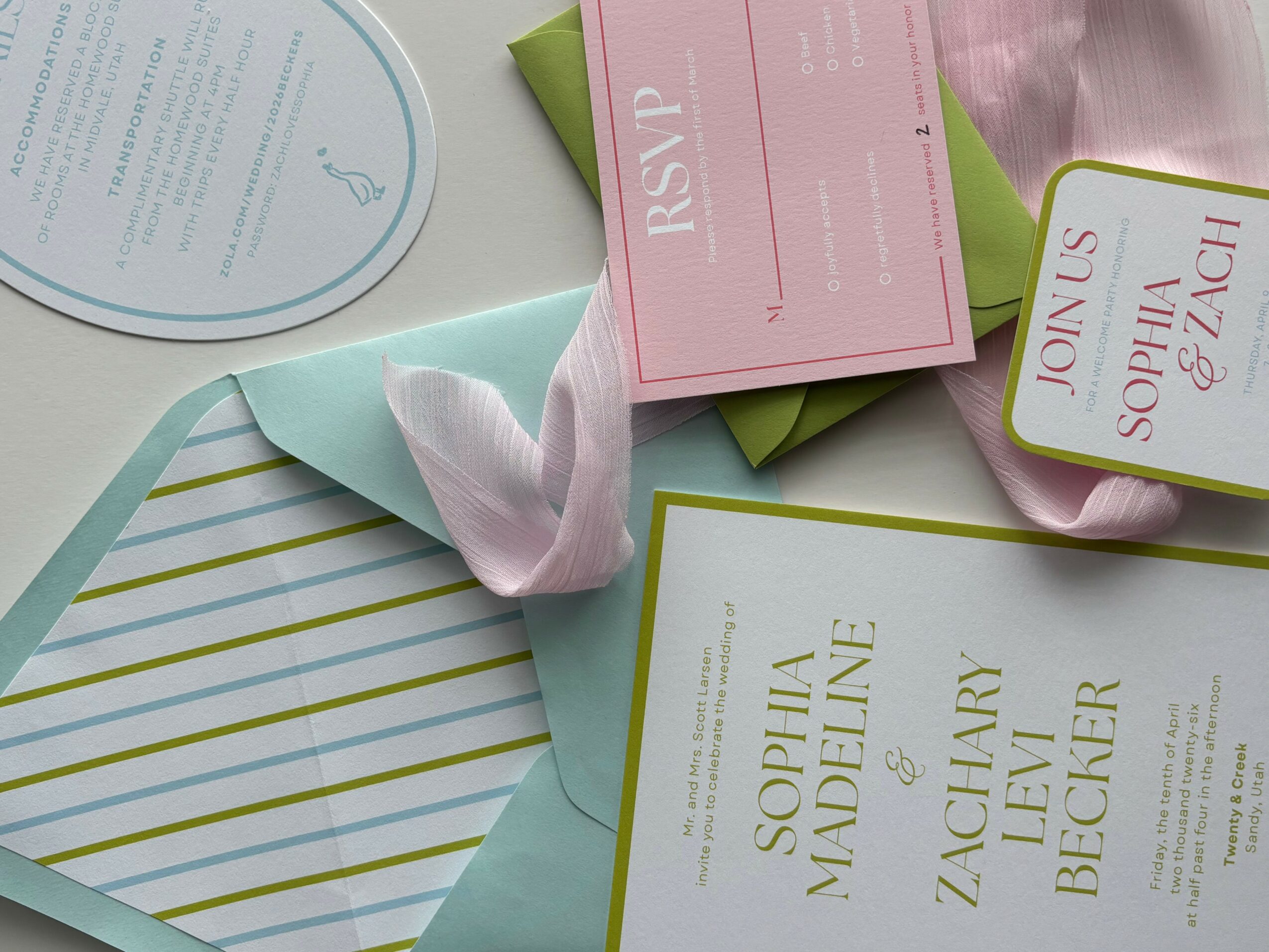 Various event invitations and RSVP card on a table, with a pink ribbon and striped paper, in soft pastel colors.