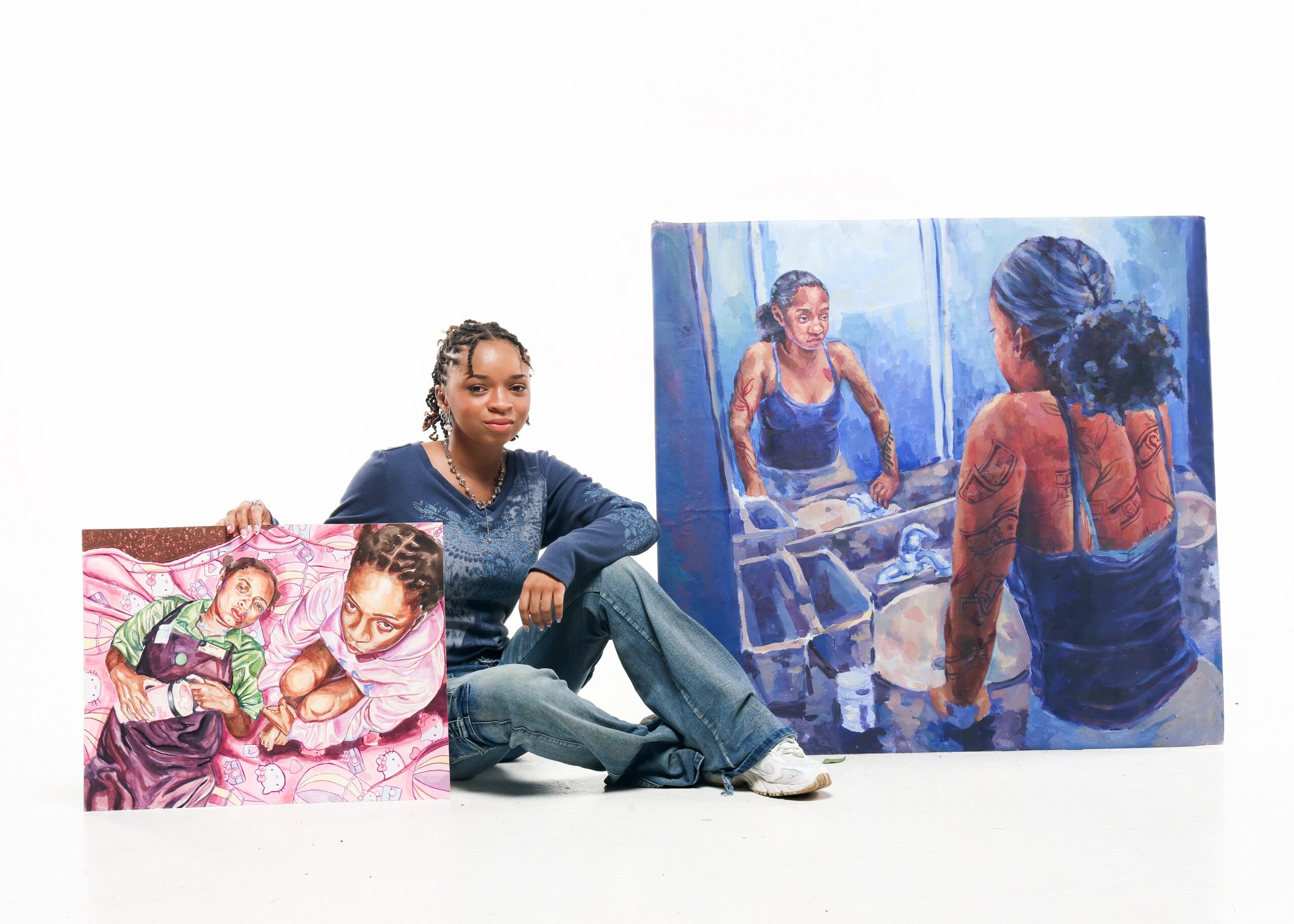 Woman sitting on the floor with two paintings of women, one large and one small, against a white background.