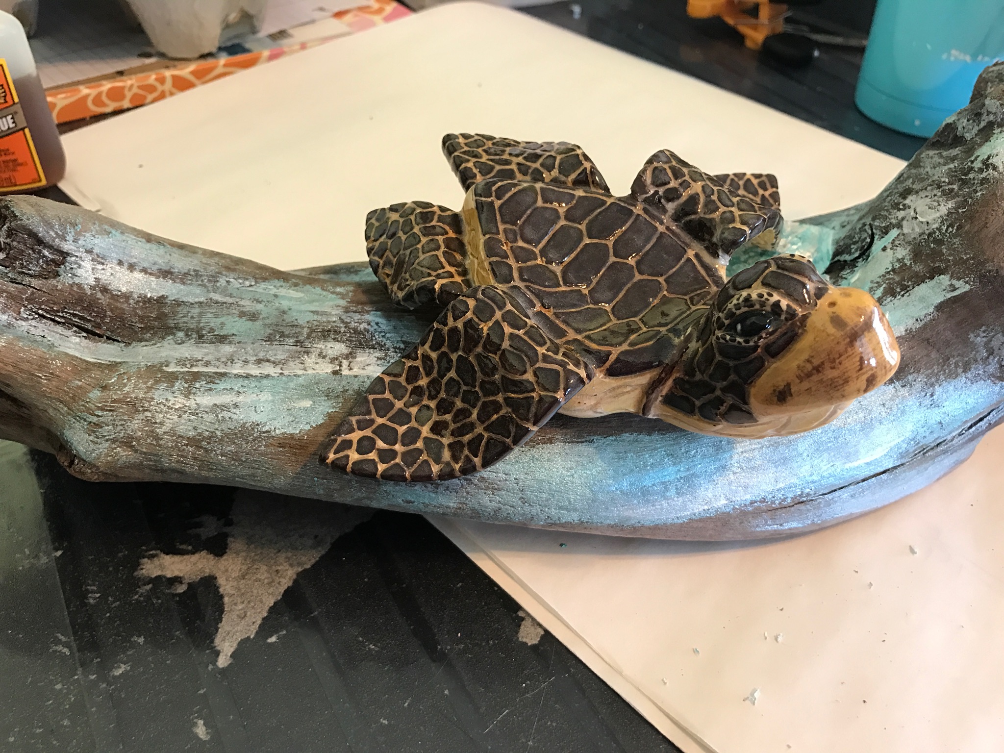 A turtle with patterned shell resting on a curved, textured surface, surrounded by various objects on a table.