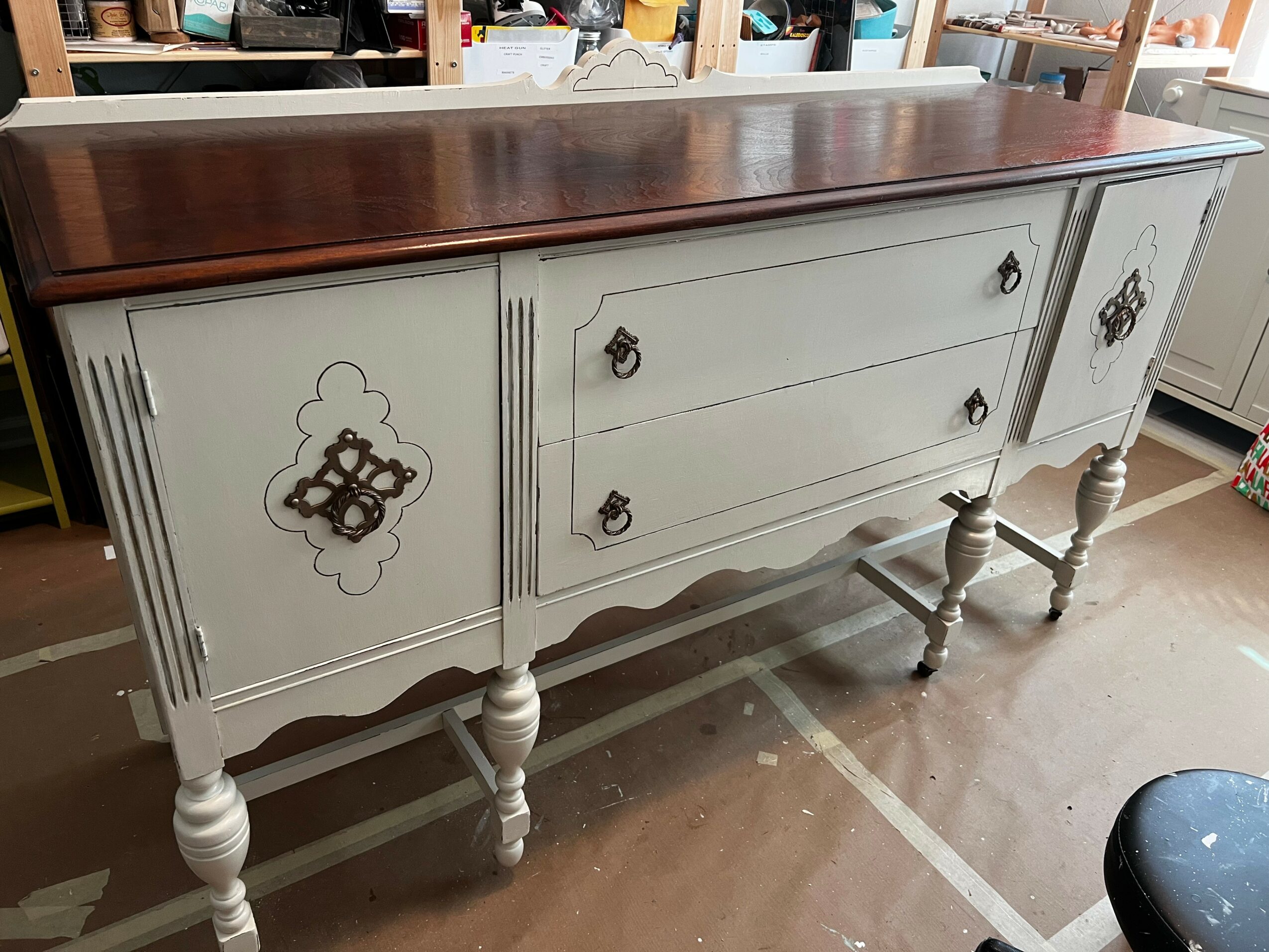 Long vintage sideboard with white painted body, dark wooden top, decorative hardware, and turned legs, in a room setting.