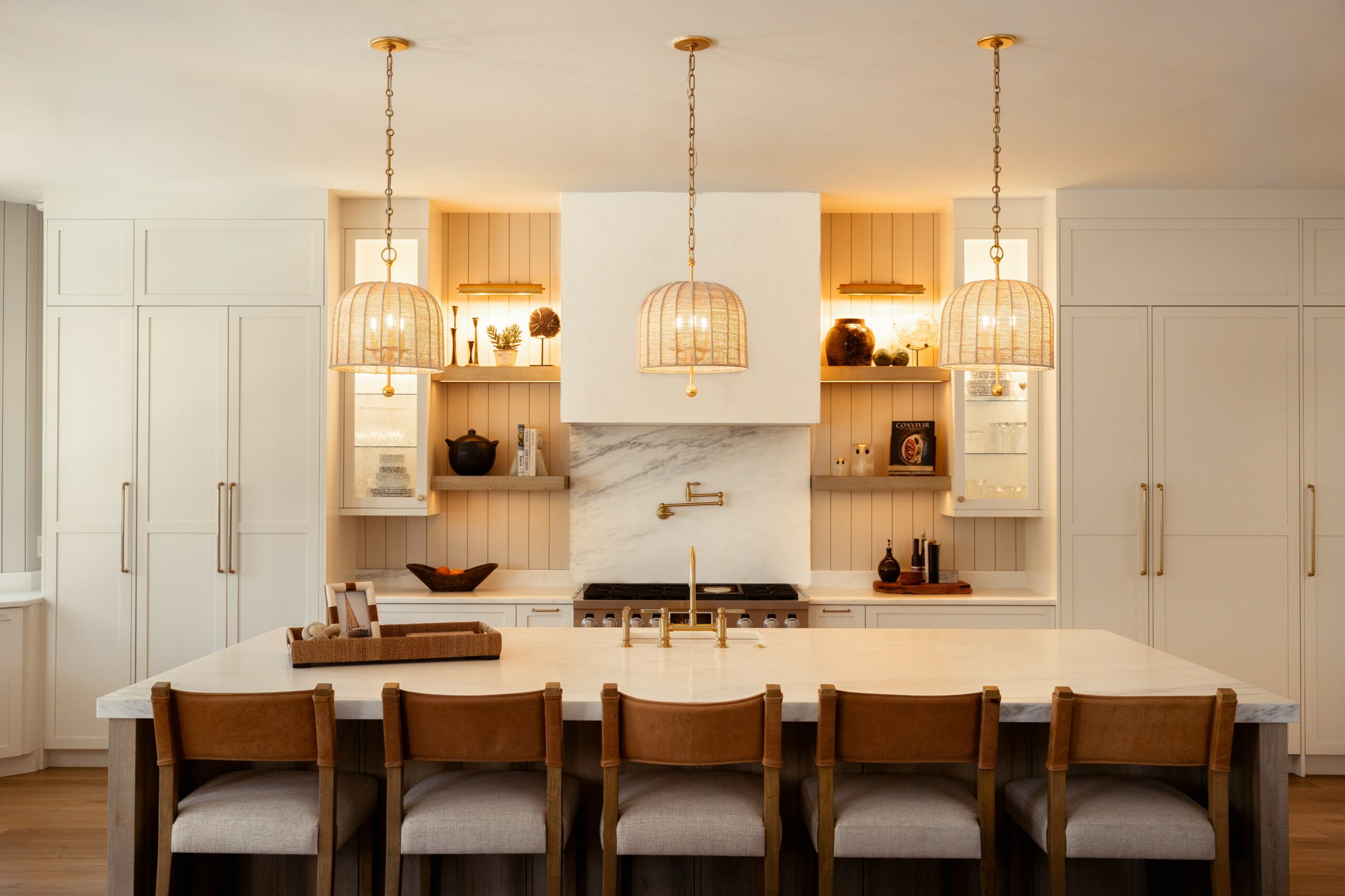 Modern kitchen with white cabinets, wooden open shelves, pendant lights, and a large island with six chairs.