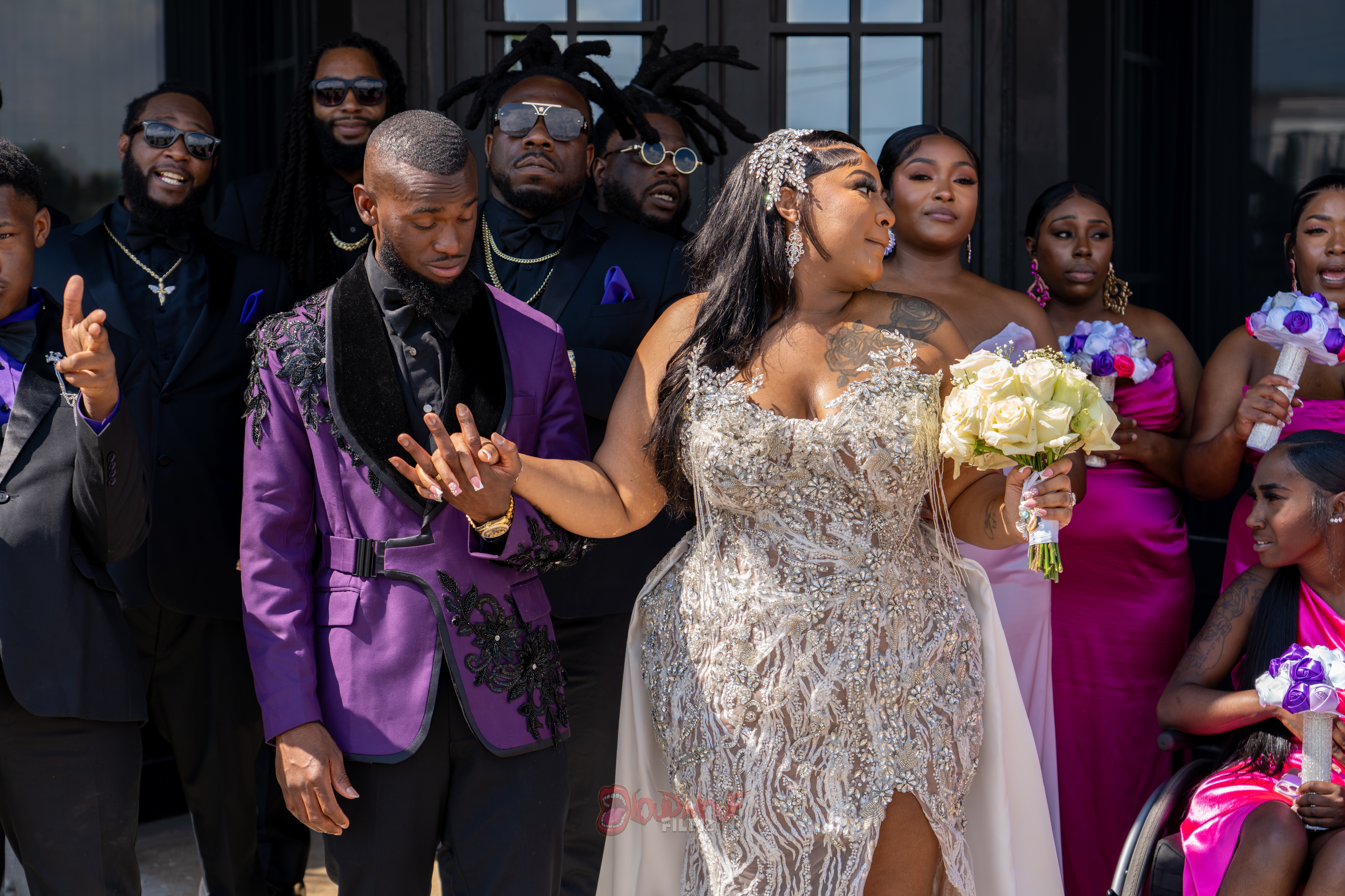 A bride in a silver gown holding a bouquet stands among guests at a wedding celebration.