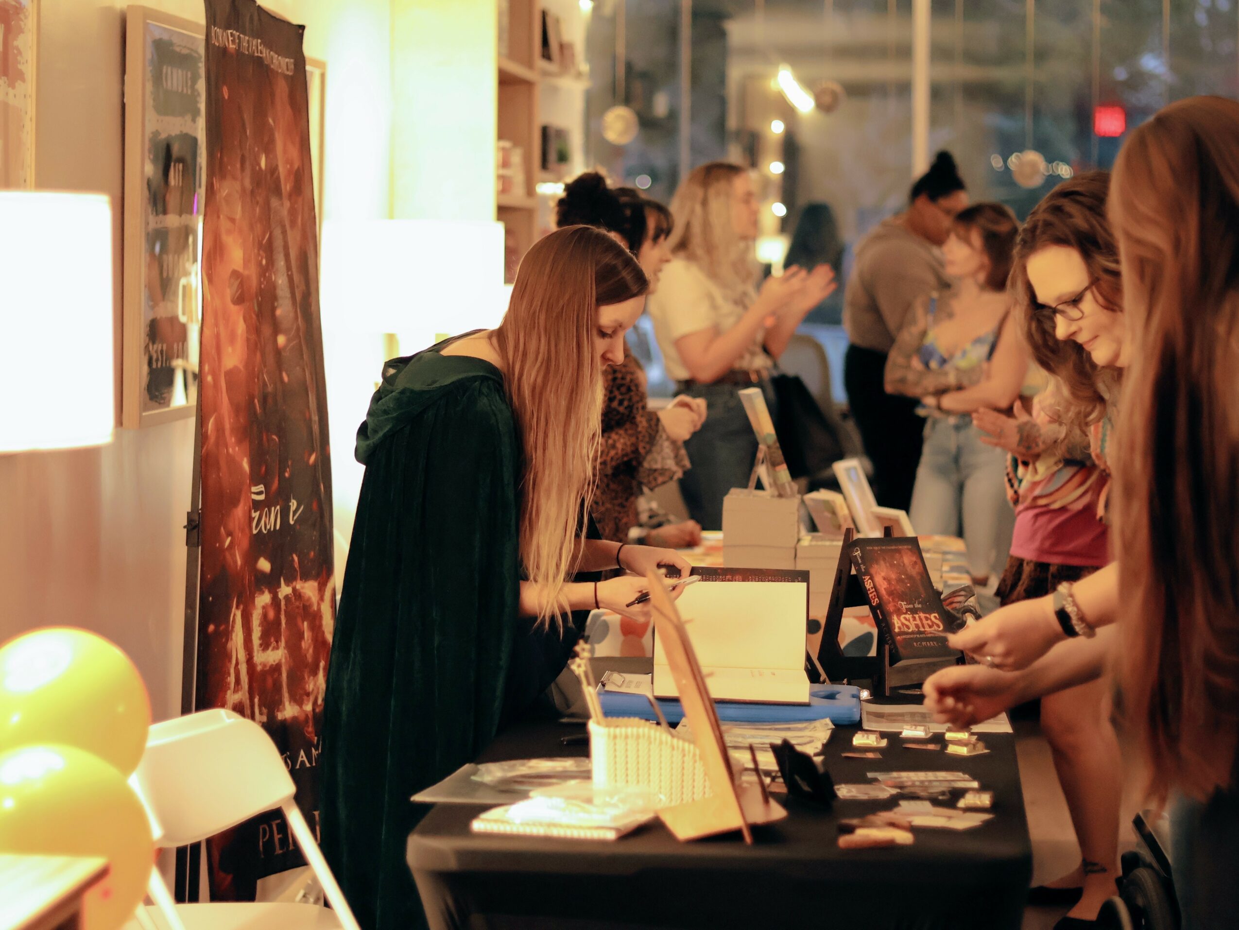 People browsing items at a store or market, with a woman in a dark coat looking at products on a table, surrounded by others.