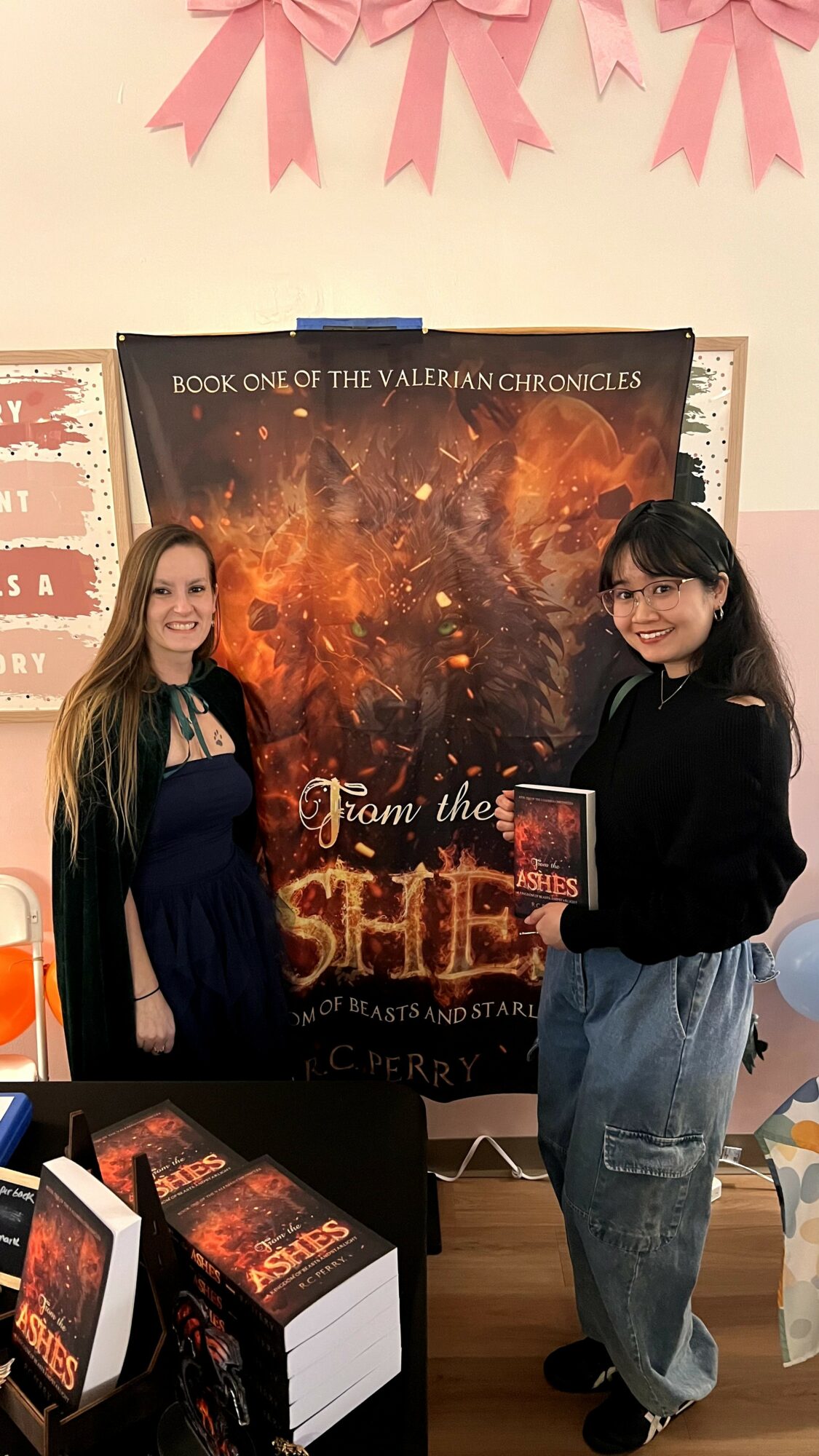 Two women standing in front of a large poster for a book titled 'From the Shadow' in a classroom or library setting.