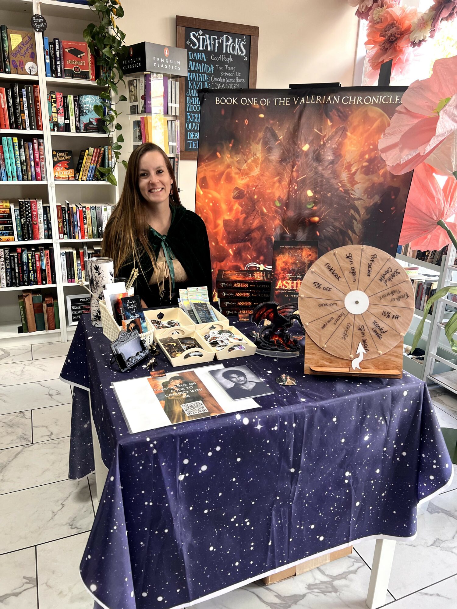 Woman standing behind a table with books and merchandise in a bookstore, space-themed display with a starry tablecloth and a large poster.