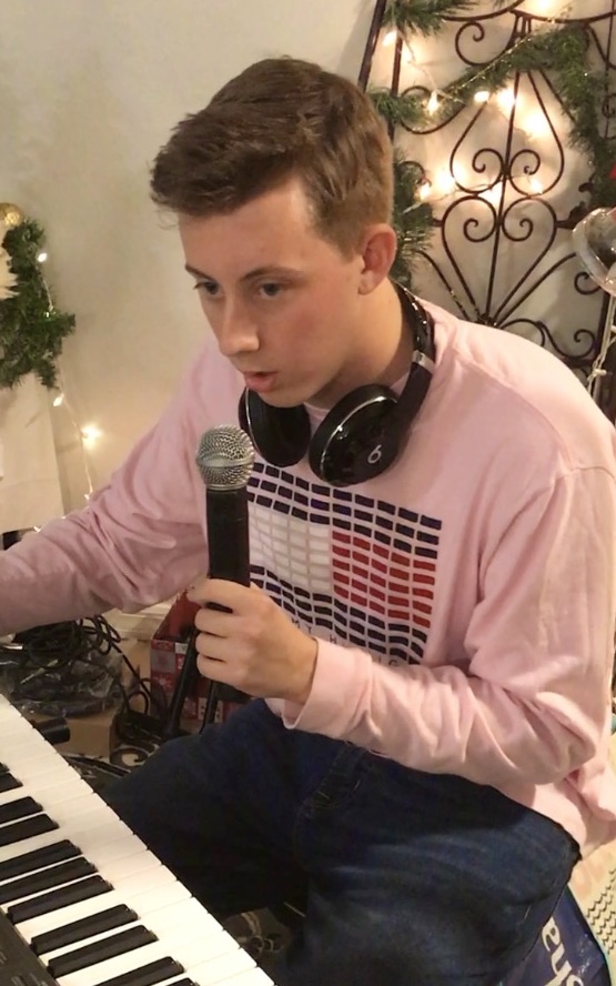 Young person with headphones around neck playing keyboard, focused, in festive setting with Christmas decorations.