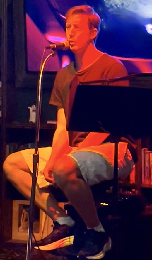 Person sitting on a chair, singing into a microphone on stage with colorful lighting.