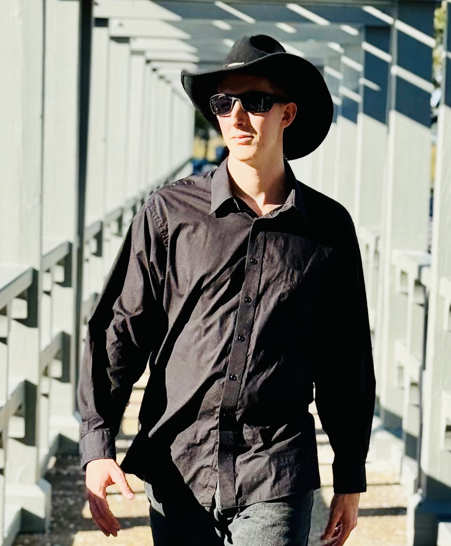 Woman wearing sunglasses, a wide-brimmed hat, and a black shirt walking outdoors on a sunny day.
