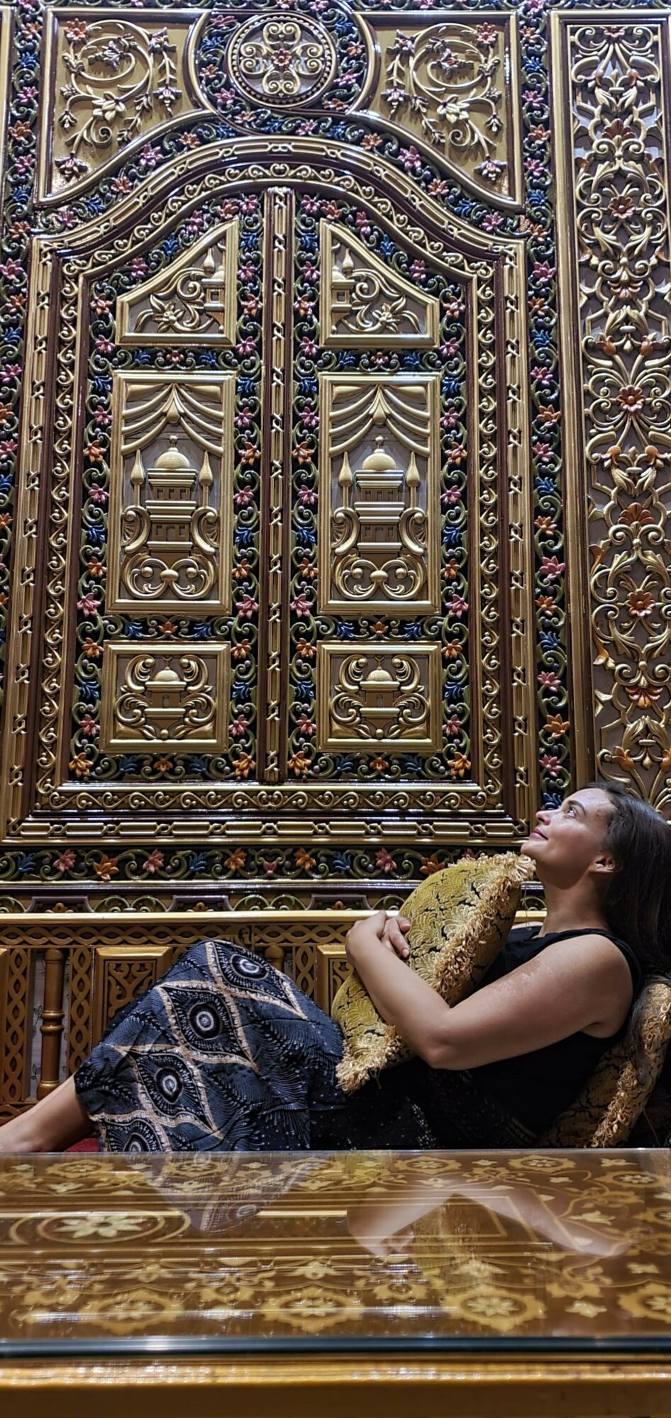 Person kneeling and looking at an ornate, decorated door with intricate patterns and gold accents.