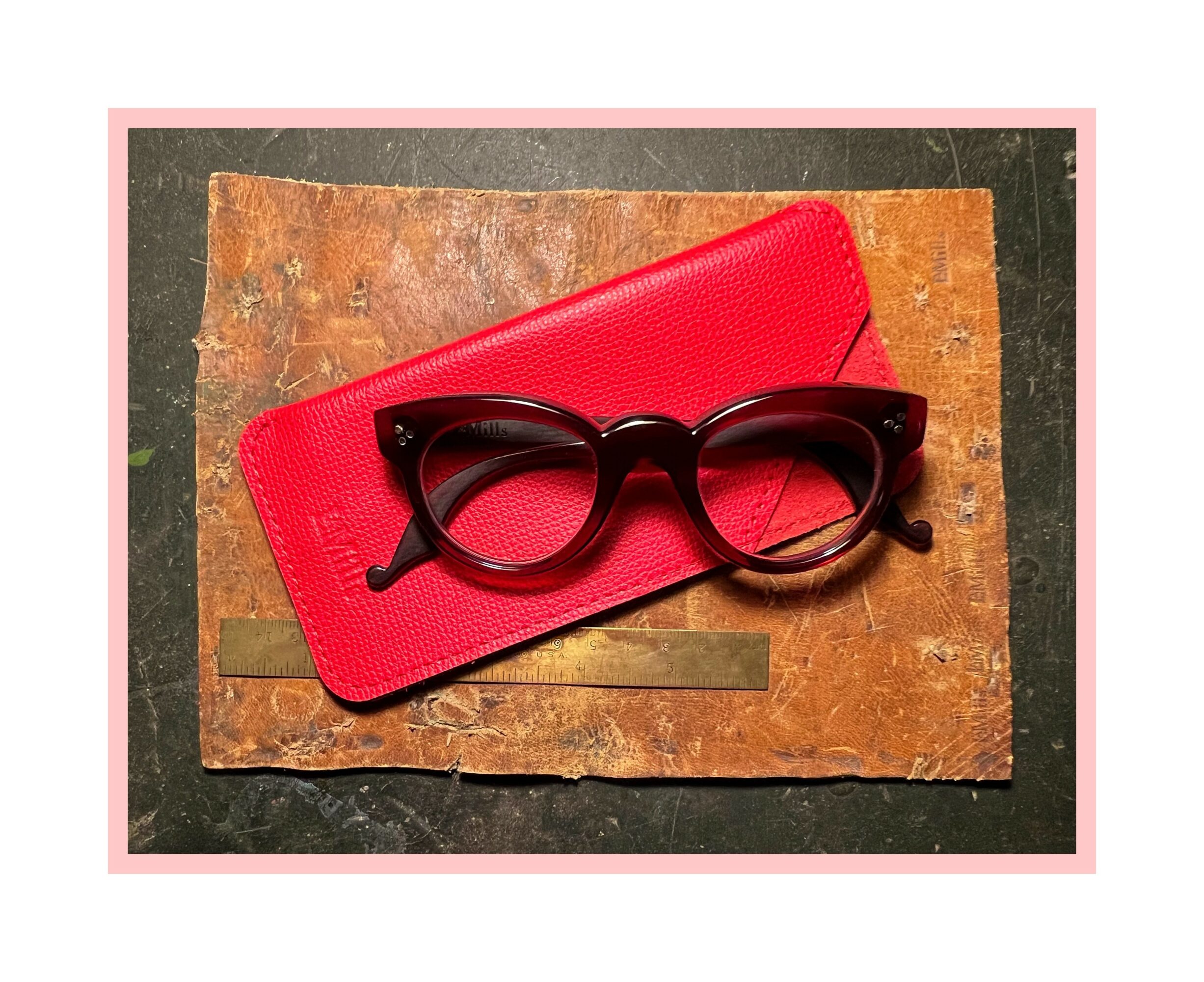 Black sunglasses resting on a red case placed on a textured brown surface.