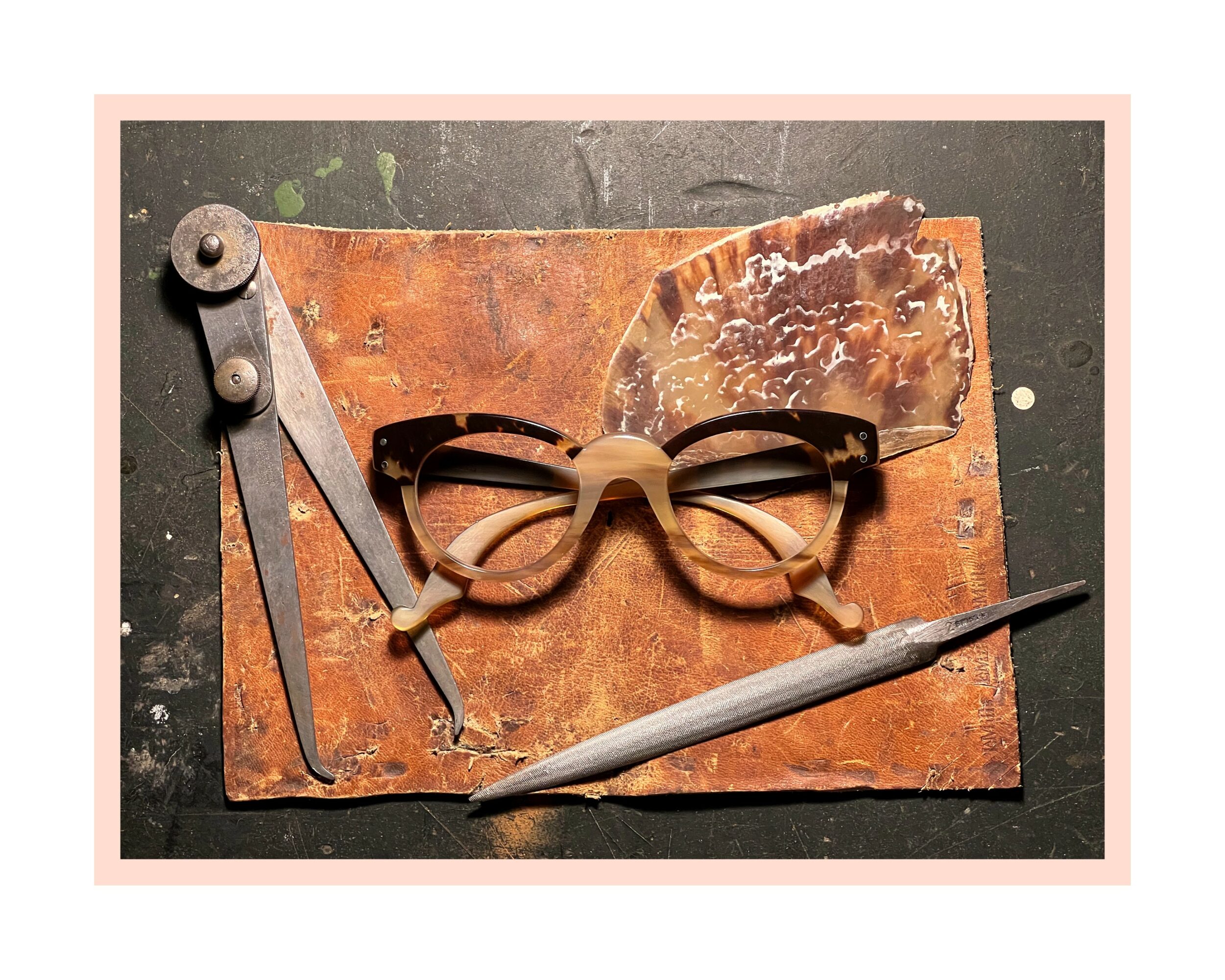 Eyeglasses, a compass, a knife, and a rusted metal piece on a wooden surface.