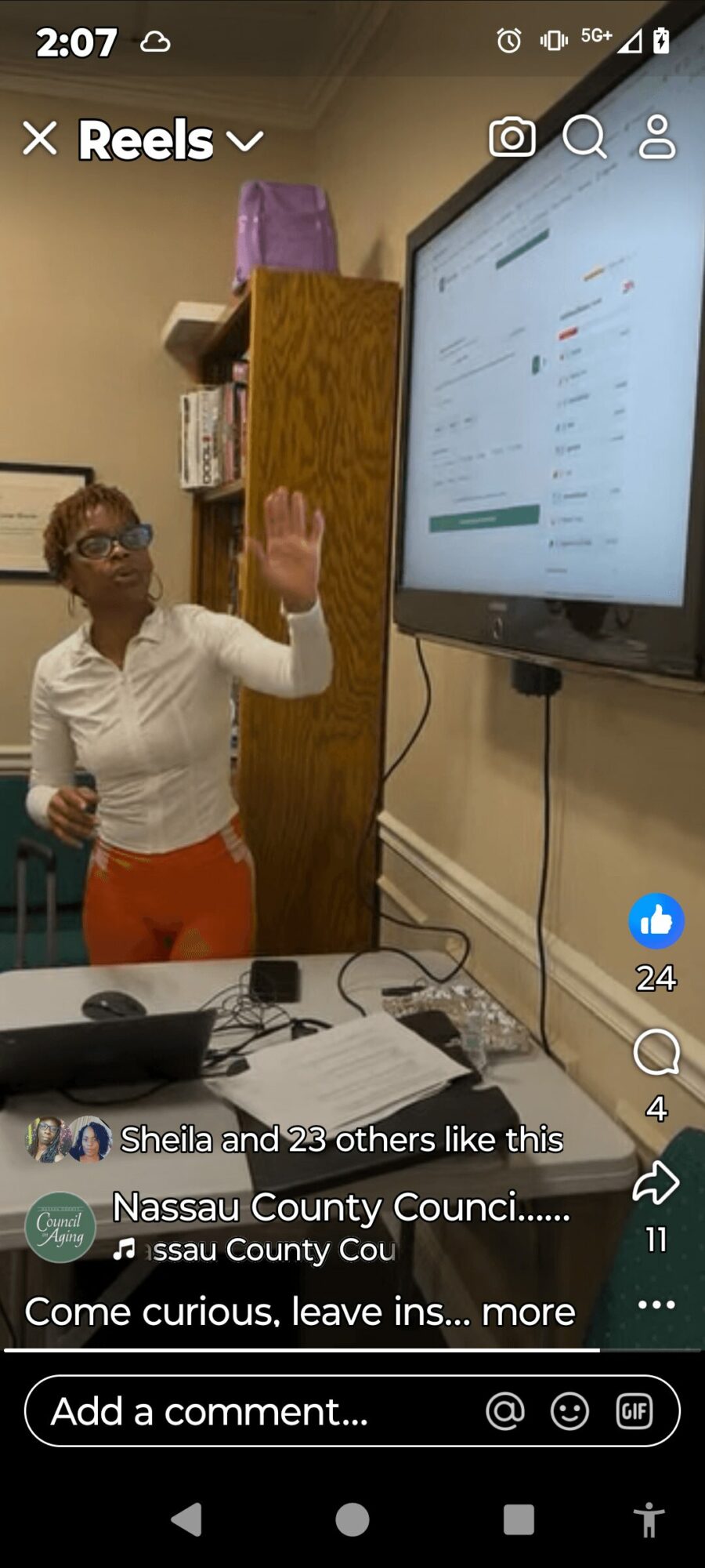 Child standing in front of a large screen, raising hand, in a classroom or office setting.