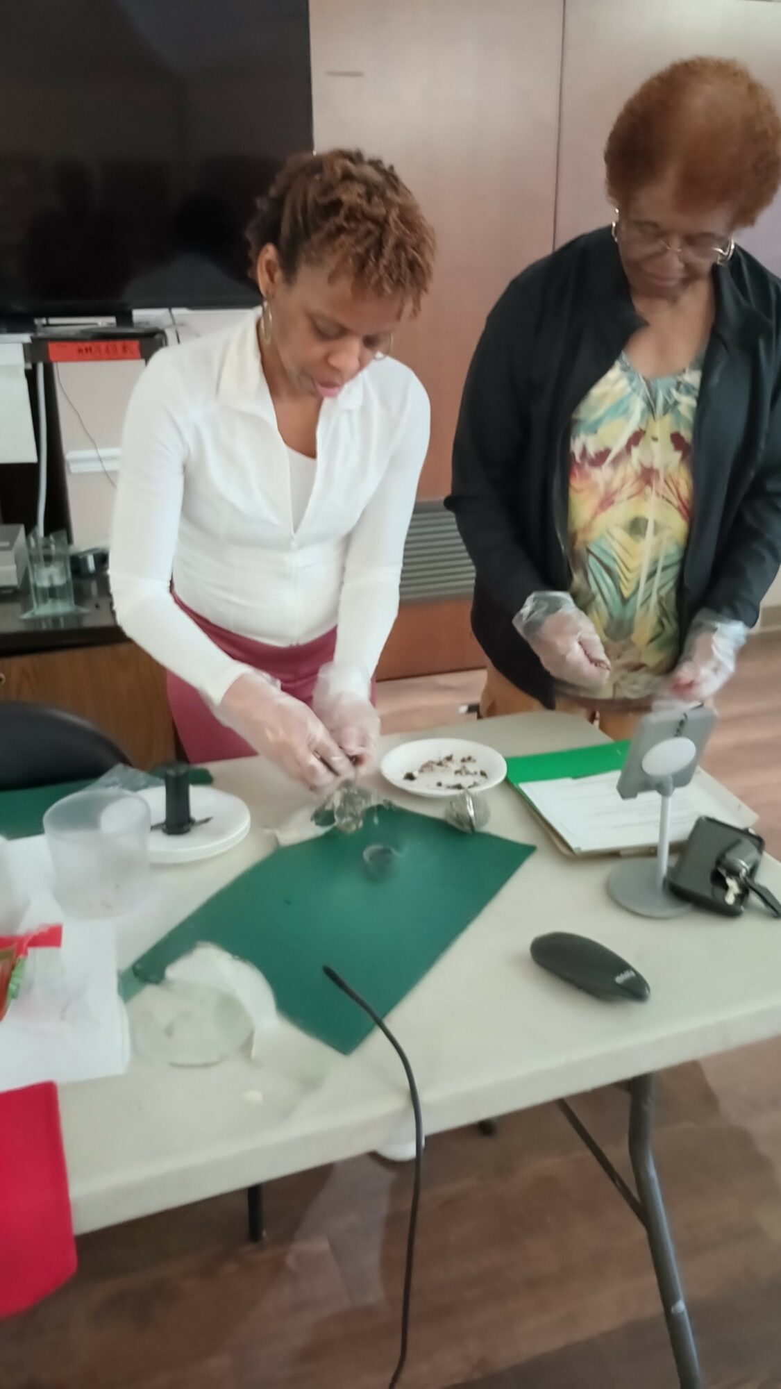 Two women working with scientific equipment at a table, one in a white shirt, the other in a dark jacket, in a room.