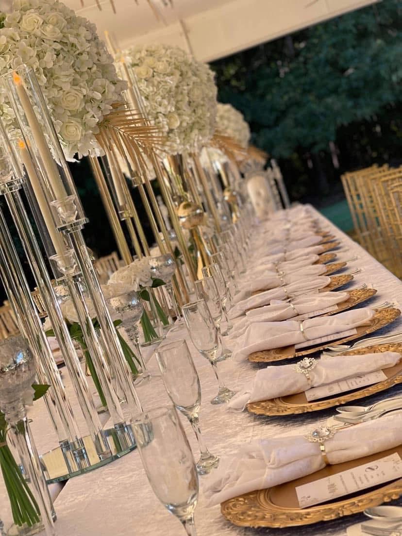Elegant table setting with gold and glass decorations, white napkins, and floral arrangements, viewed from the side outdoors.