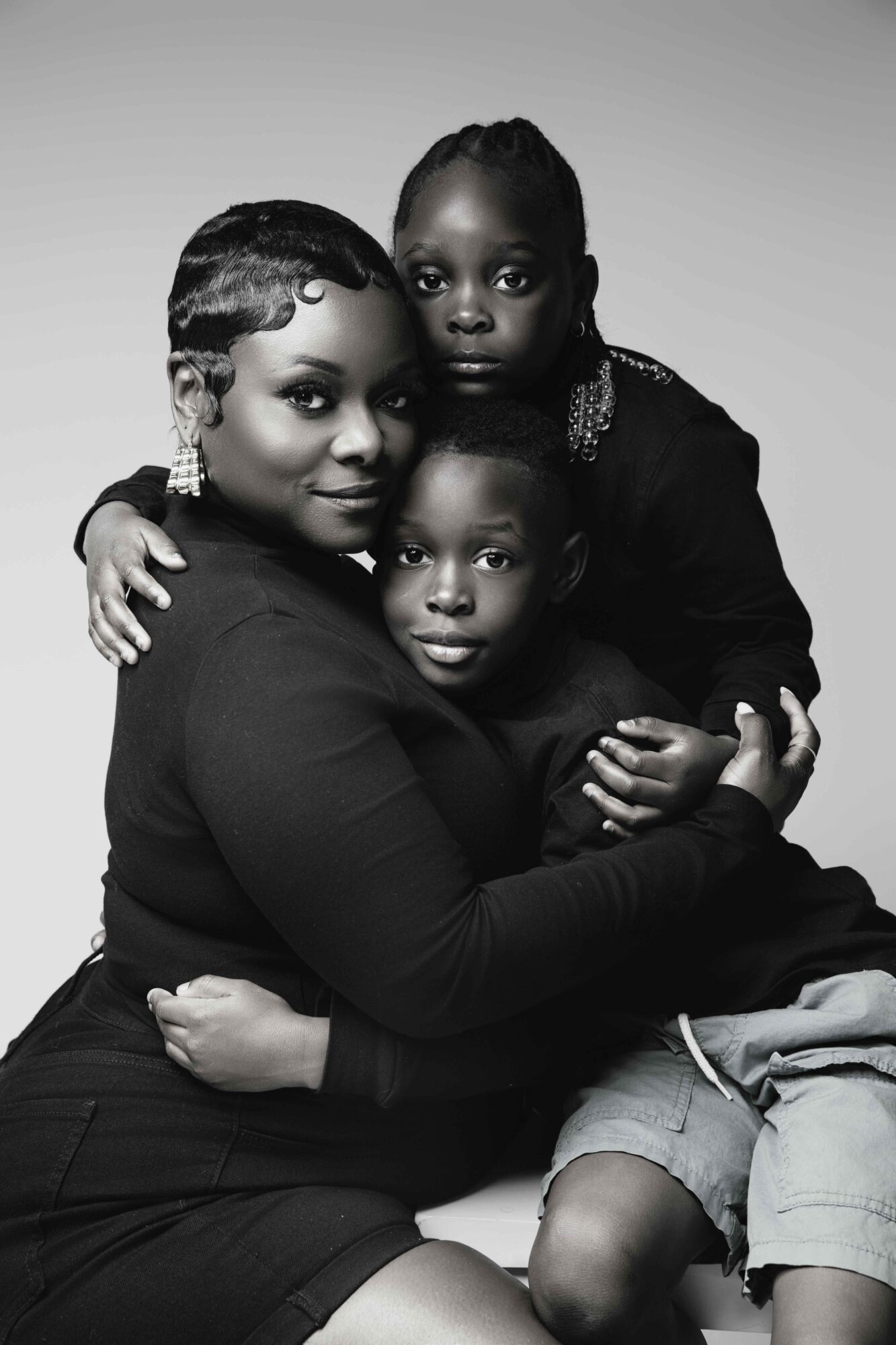 A woman with two children, all sitting closely together, with the woman holding the children on her lap, in black and white.