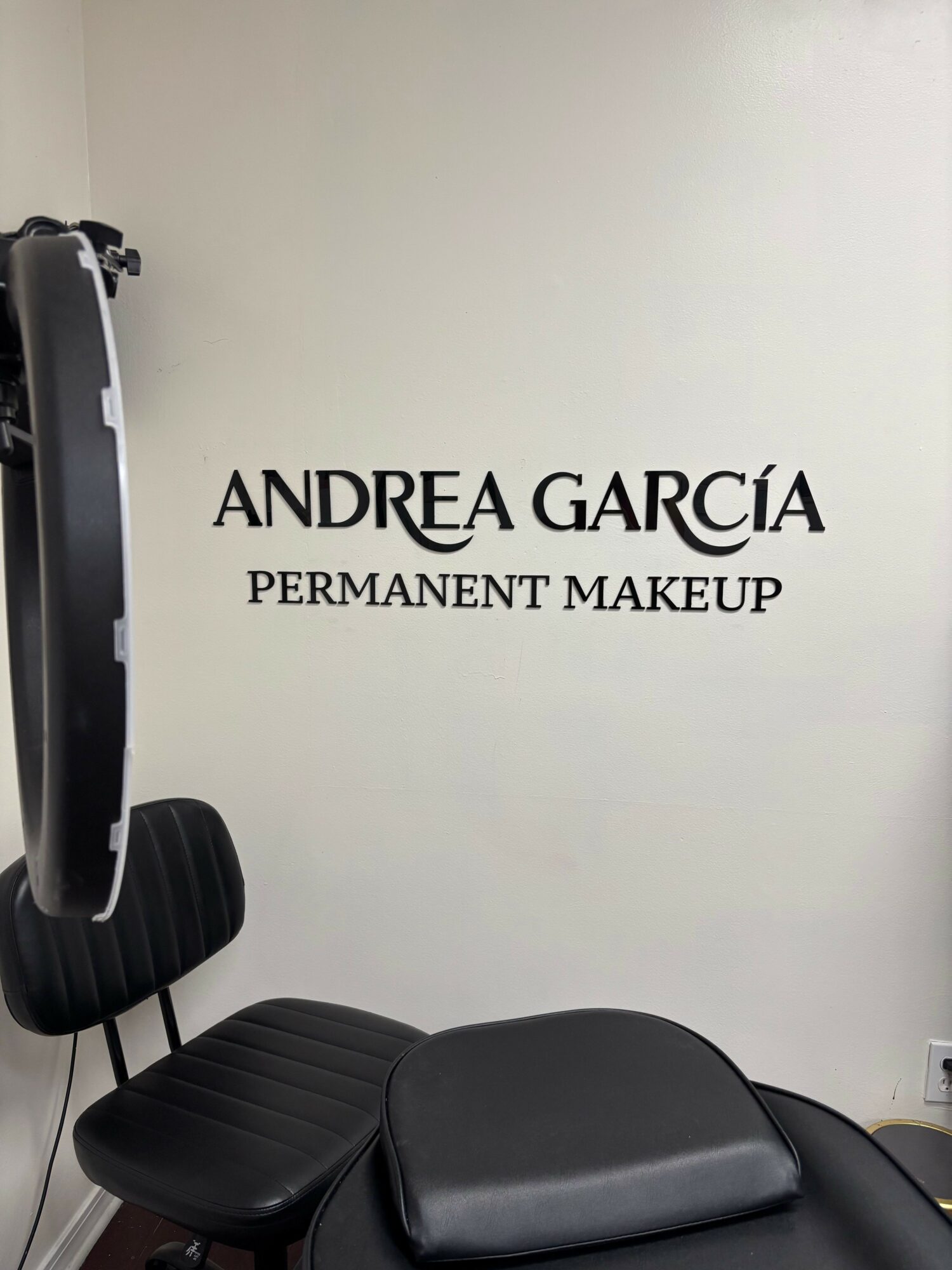 Wall with text 'ANDREA GARCÍA PERMANENT MAKEUP' and a black chair in the foreground.