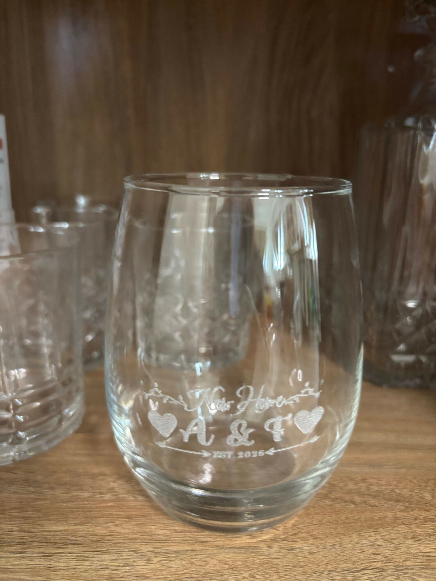Clear glass mug with white text and design, placed on a wooden surface, viewed sideways.