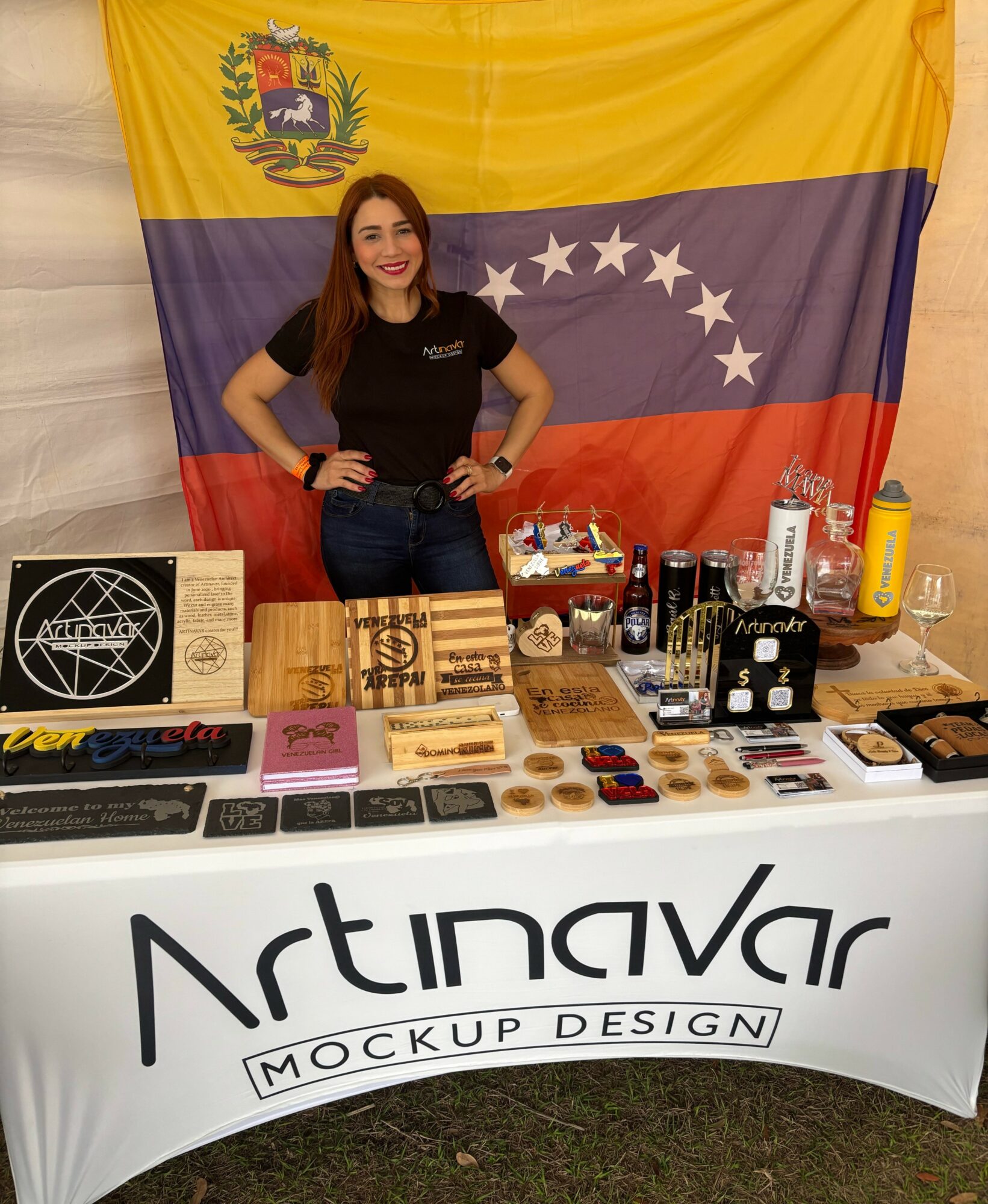 Young woman standing behind a table with Venezuelan flag in background, displaying various products and promotional materials.